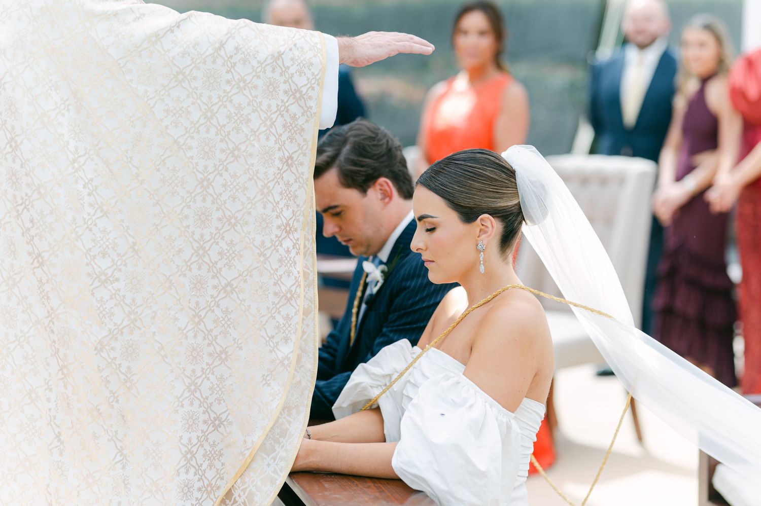 Bride and groom bowing heads in prayer under ceremonial cloth during wedding ceremony.