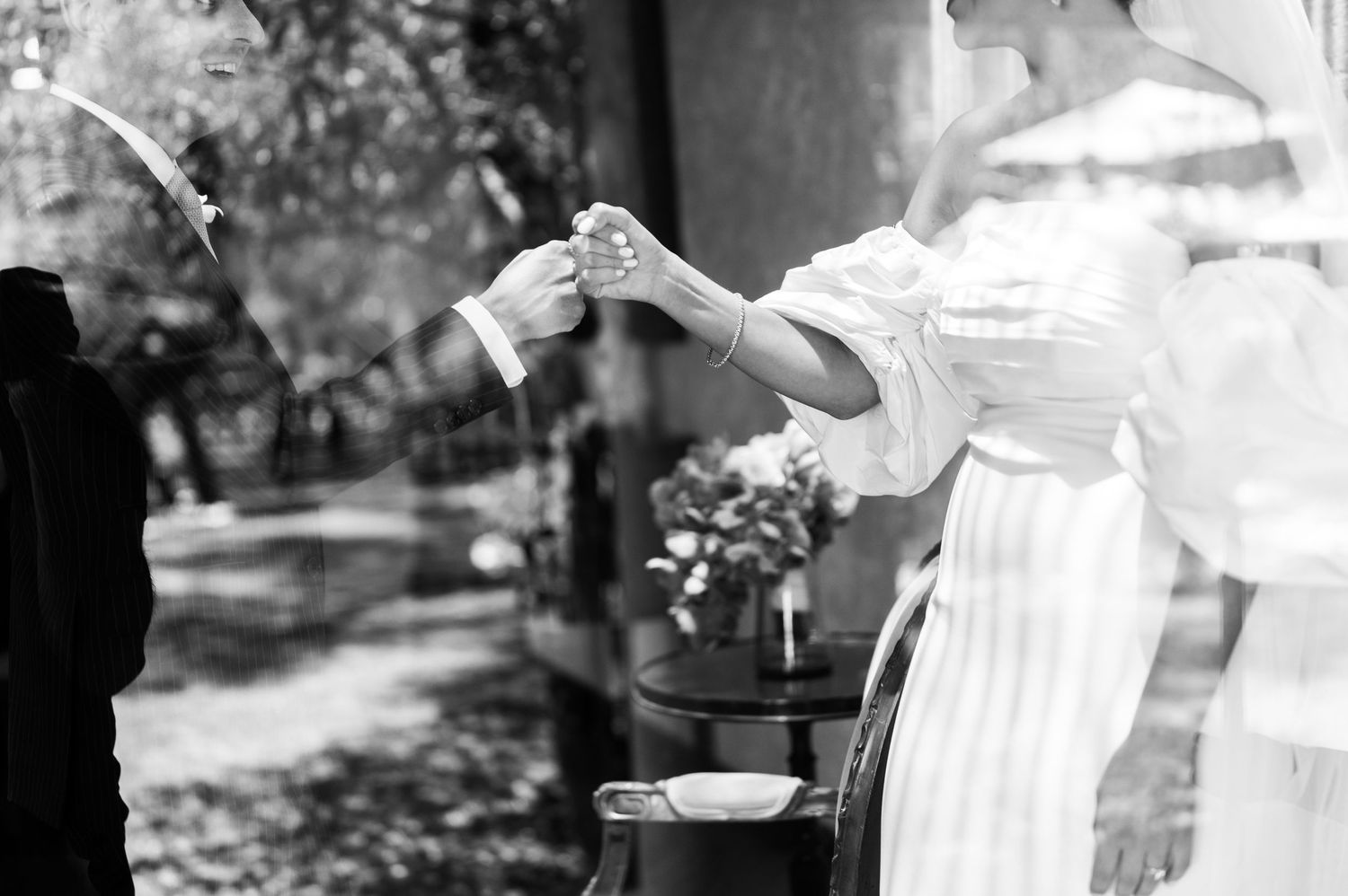 Black and white close-up of bride and groom holding hands during outdoor wedding ceremony ring exchange.