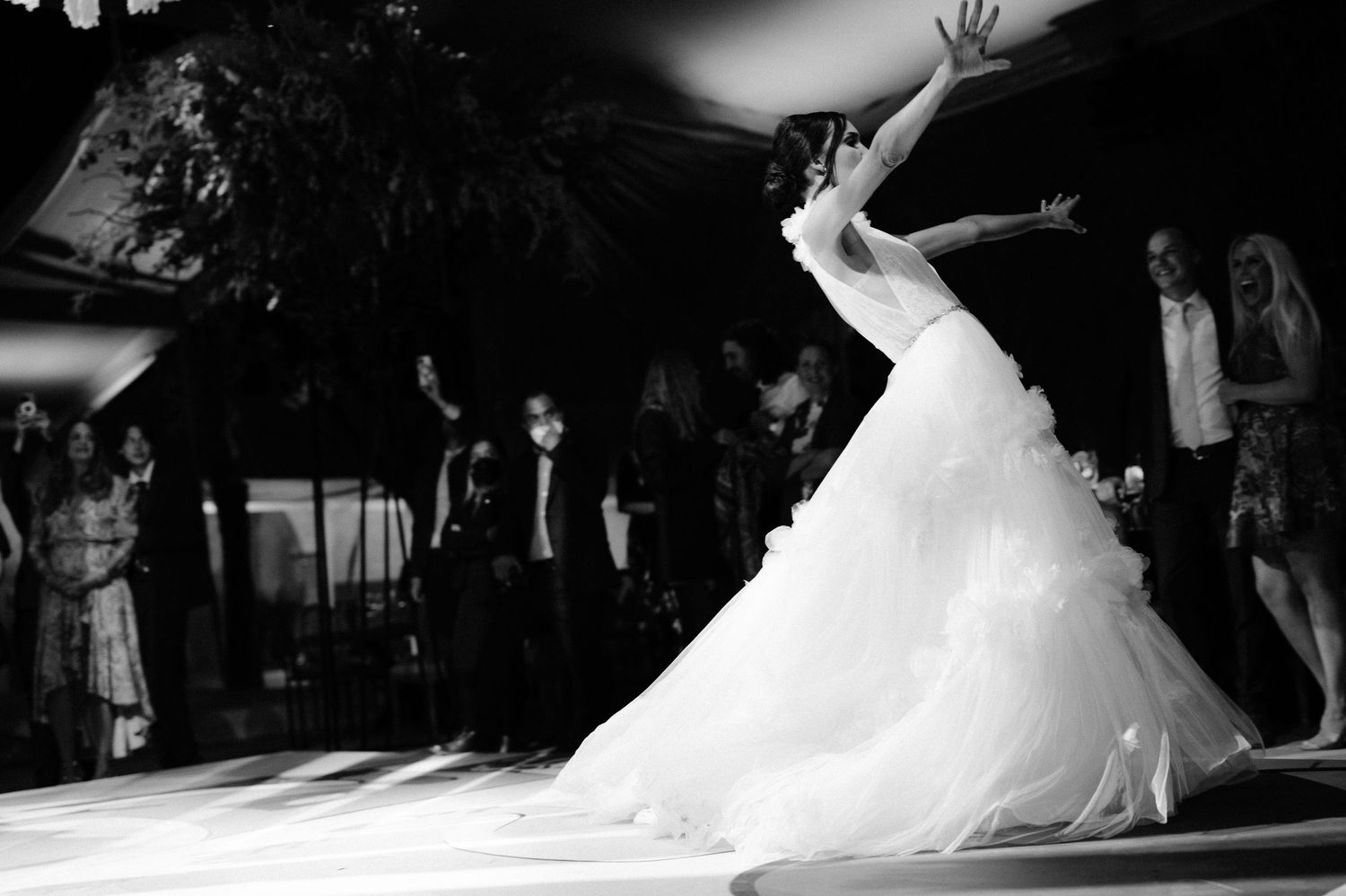 Bride twirls elegantly in white ball gown on dance floor in black and white wedding photo.
