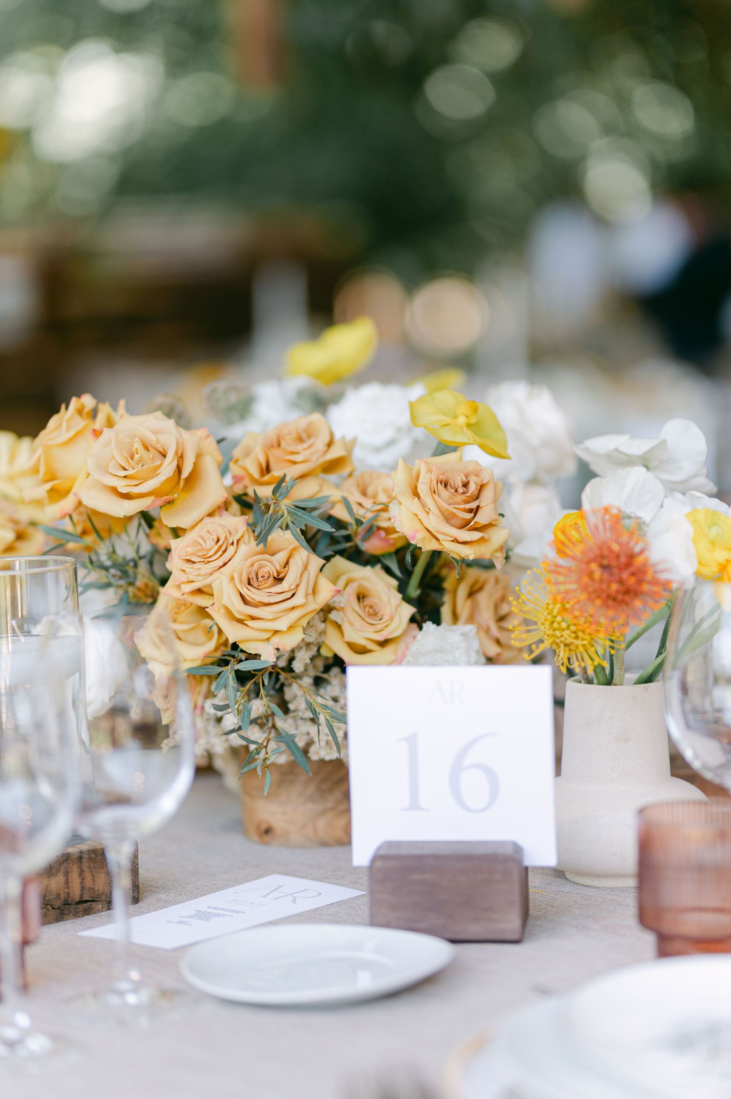 Elegant wedding table centerpiece with yellow and white roses beside table number 16 card.