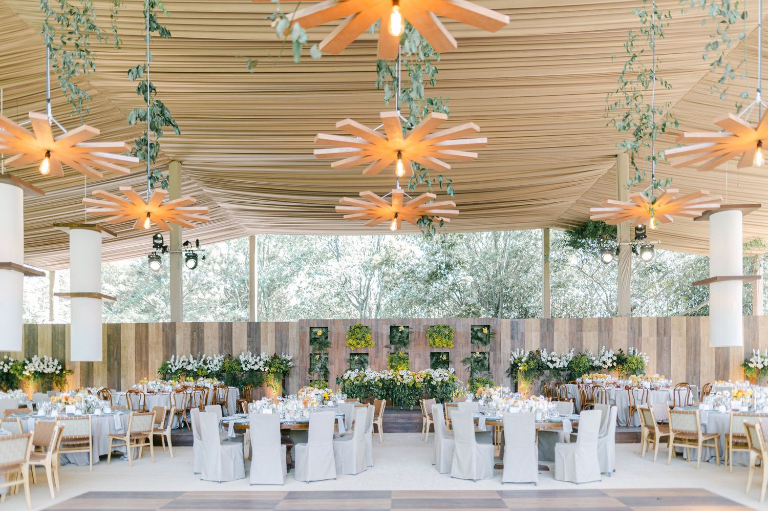 Elegant wedding reception hall with round tables, gray linens, and hanging greenery decor.