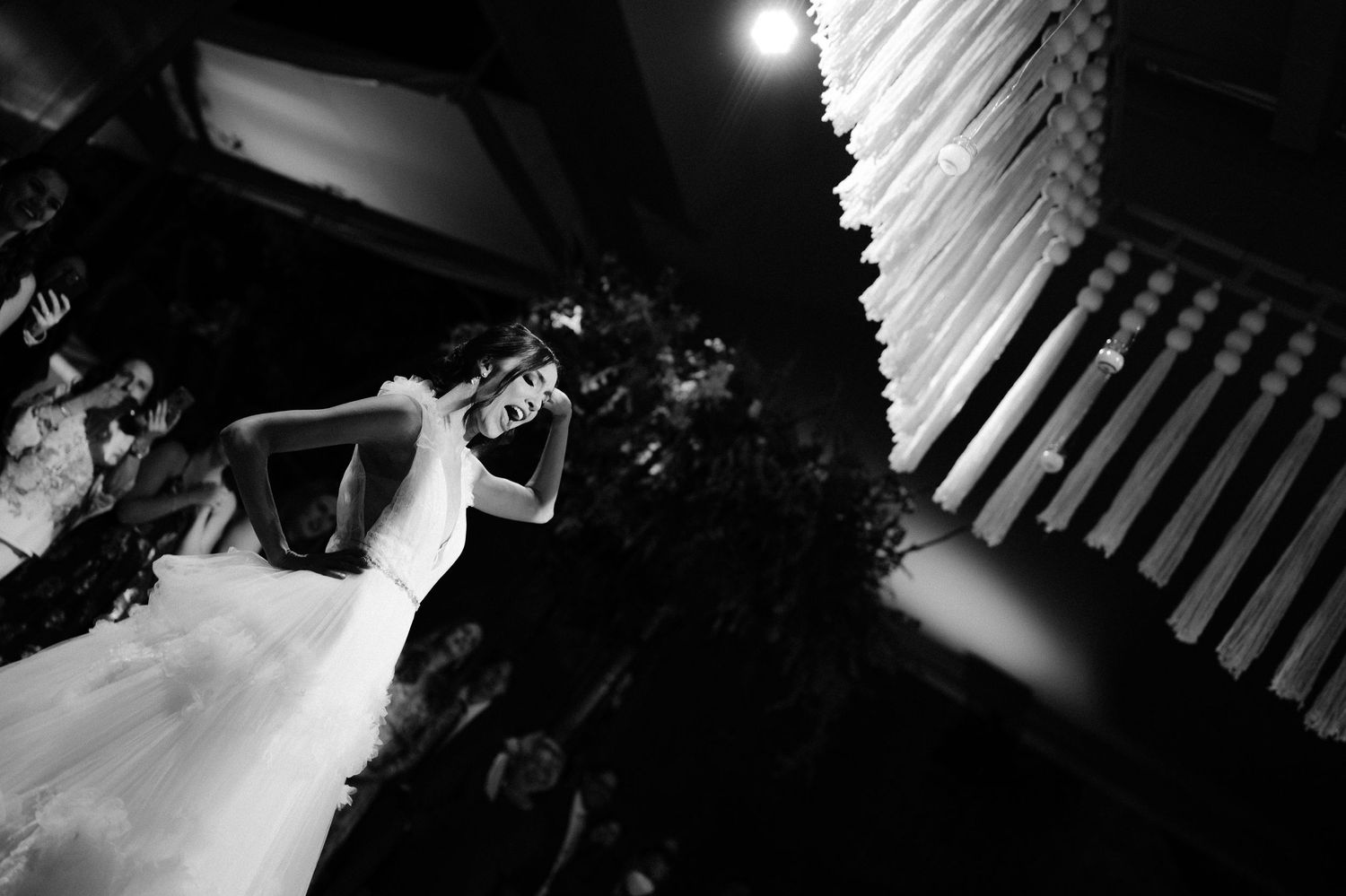 Dramatic black and white photo of bride in white gown dancing beneath hanging installation at reception.