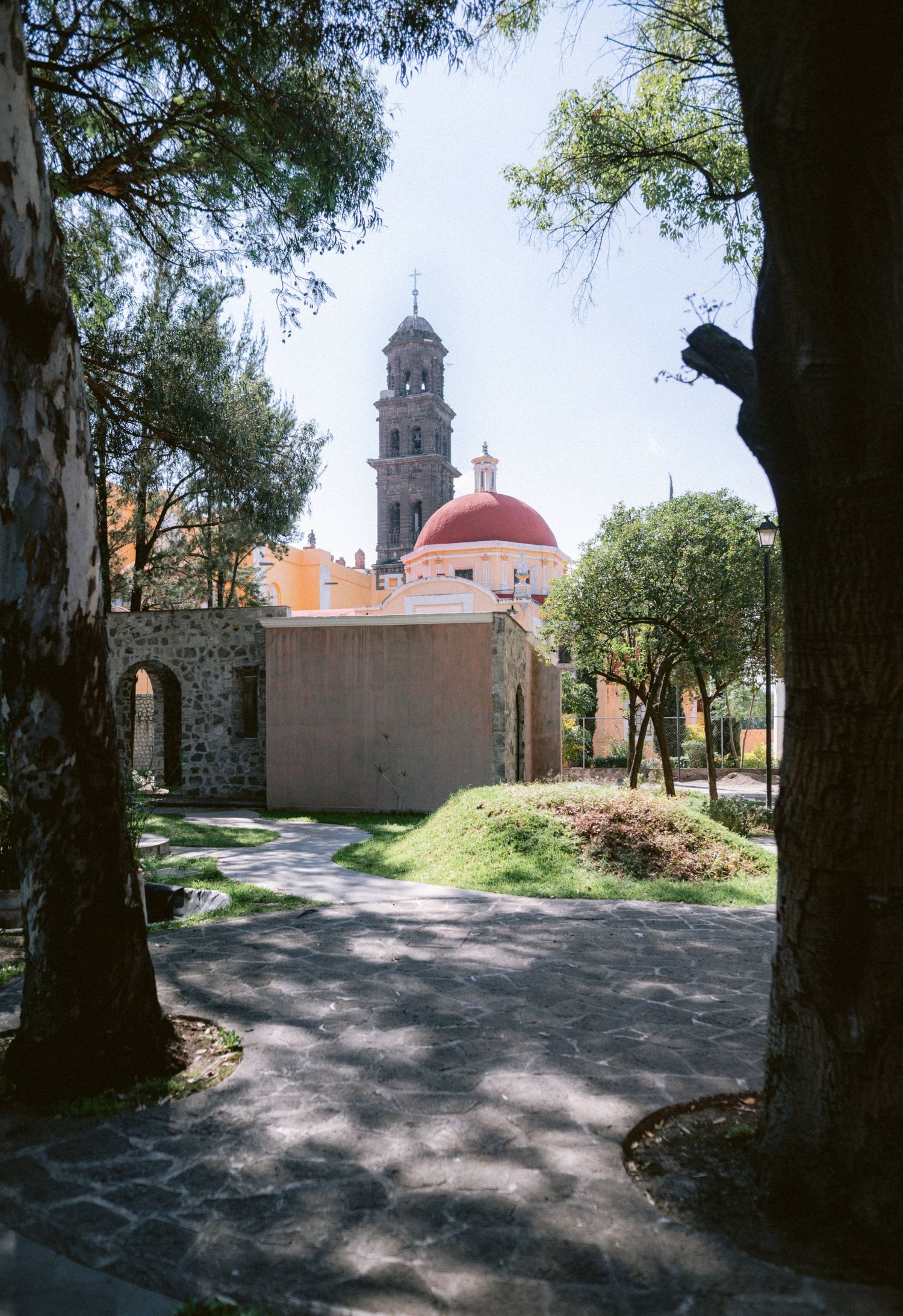 Scenic view of historic Mexican church with red dome and bell tower framed by tall trees.
