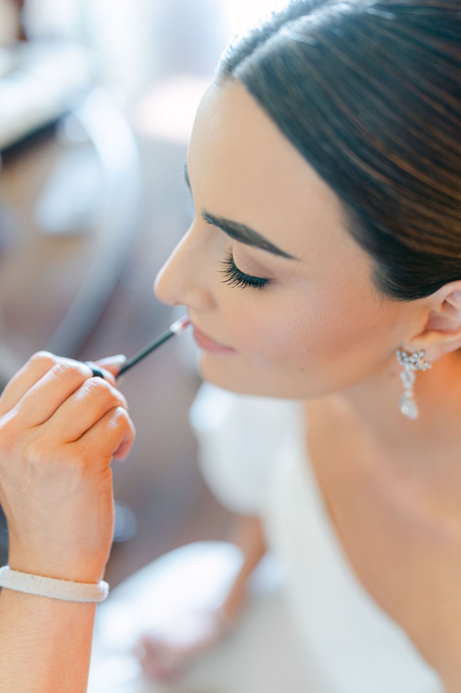 Close-up of bride receiving makeup application, wearing crystal drop earrings and natural bridal beauty look.