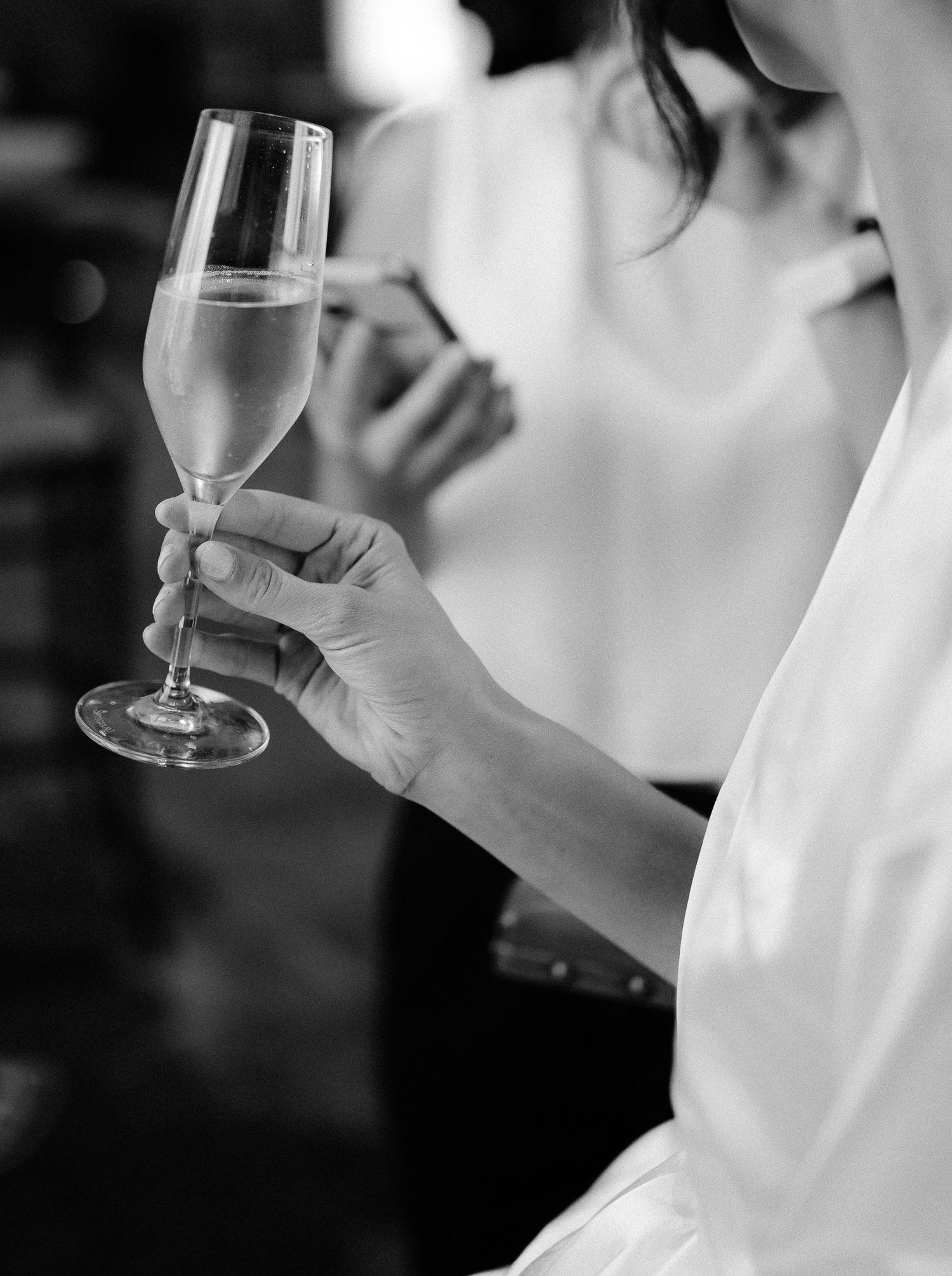 Bride in white robe holding champagne flute in elegant black and white wedding preparation photo.