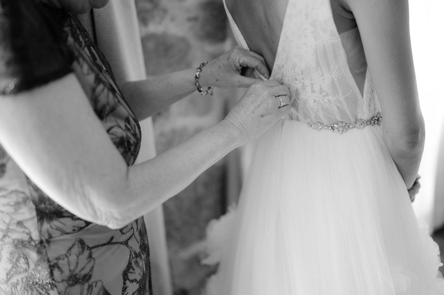 Close-up black and white photo of hands fastening bride's beaded wedding gown belt.