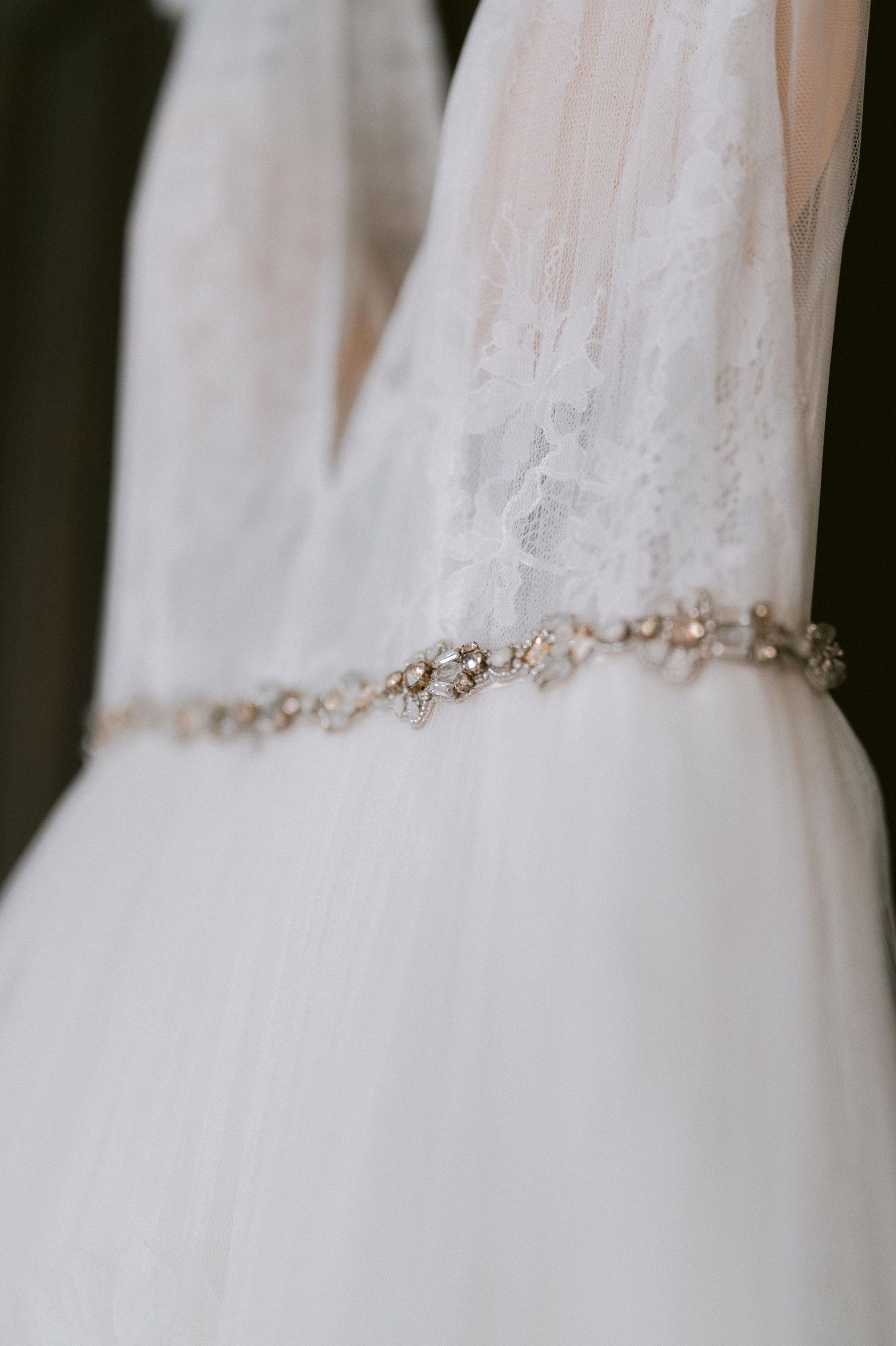 Close-up of a white wedding dress bodice with delicate lace and a crystal beaded belt detail.