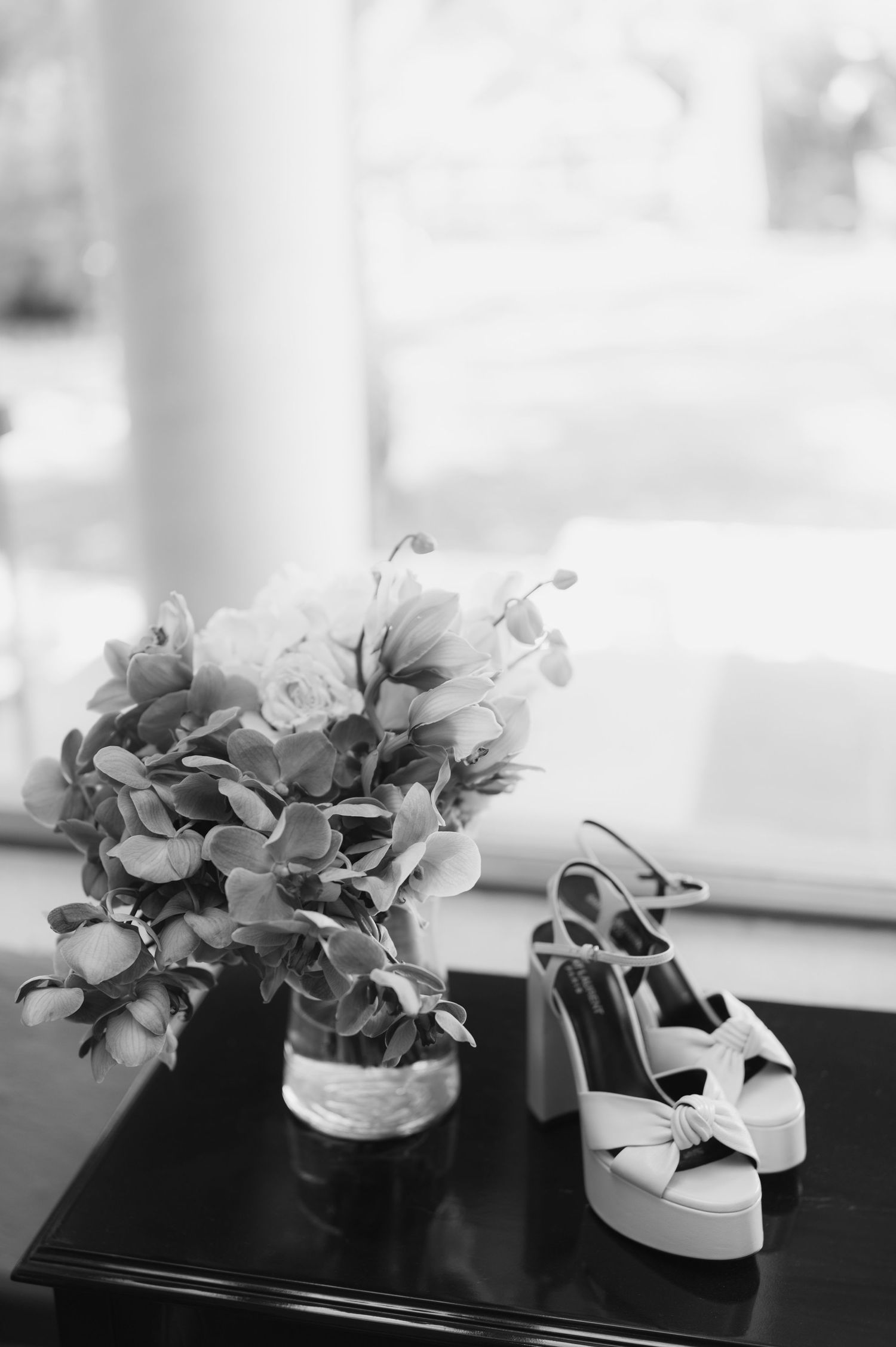 Black and white photo of a bridal bouquet with hydrangeas beside platform heeled wedding shoes.
