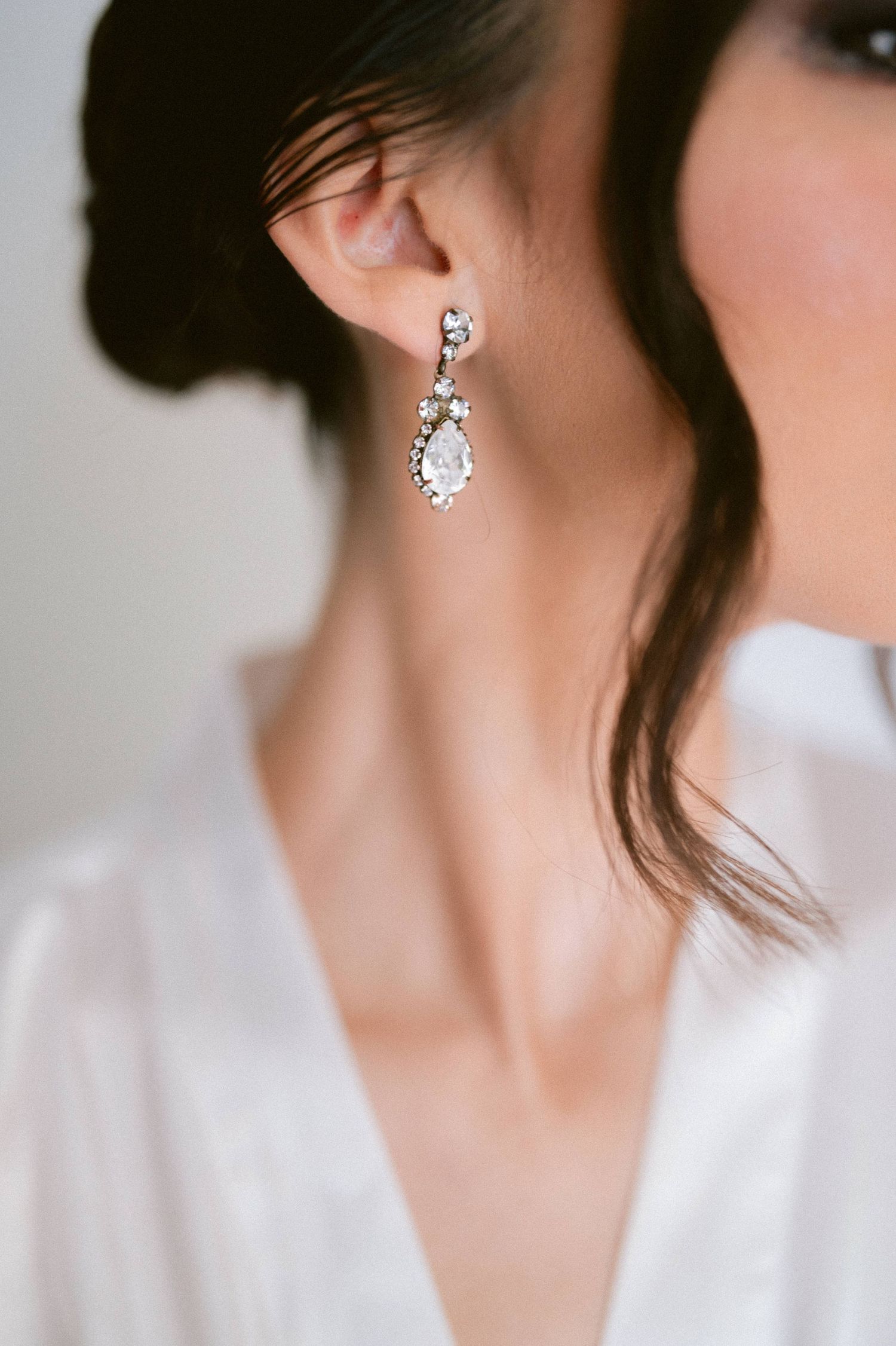 Close-up of a bride wearing an elegant crystal teardrop drop earring with dark hair updo.