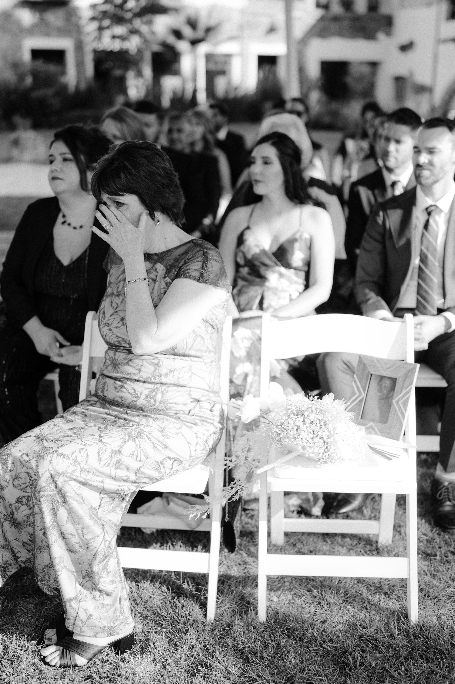 Emotional wedding guest wipes tears while seated among other guests during outdoor wedding ceremony.