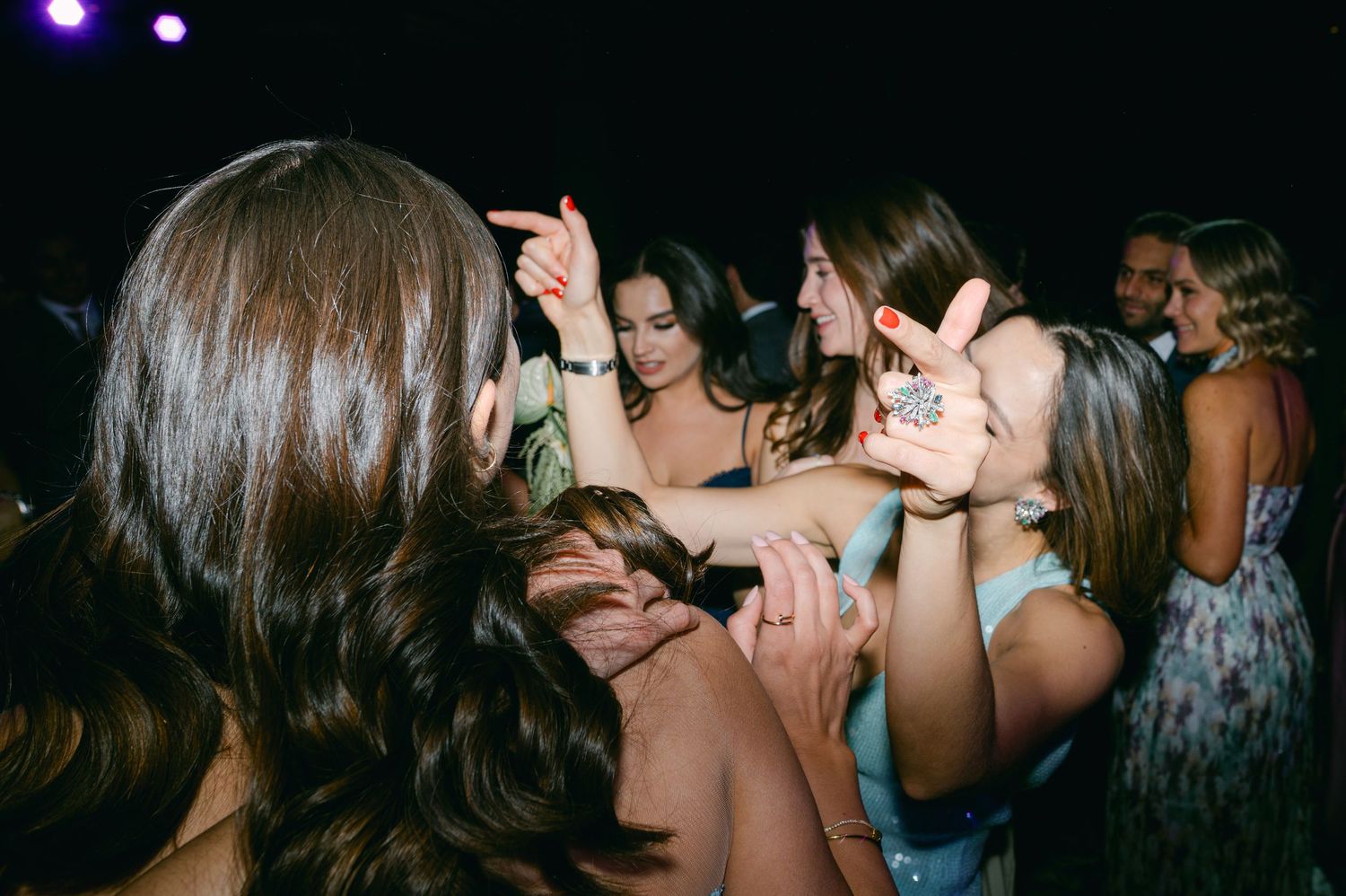 Wedding guests dancing closely together in dimly lit reception venue during energetic celebration.