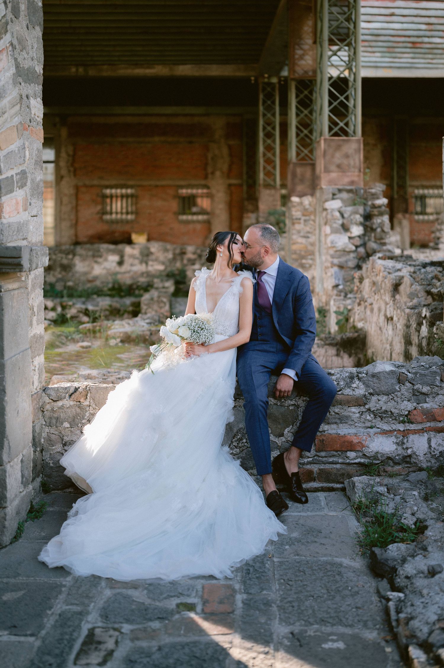 Bride and groom sharing a kiss while seated on stone steps at an ancient ruins wedding location.