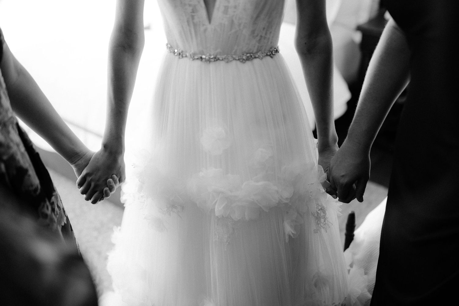 Black and white photo of bride in lace wedding gown holding hands in circle with wedding party.