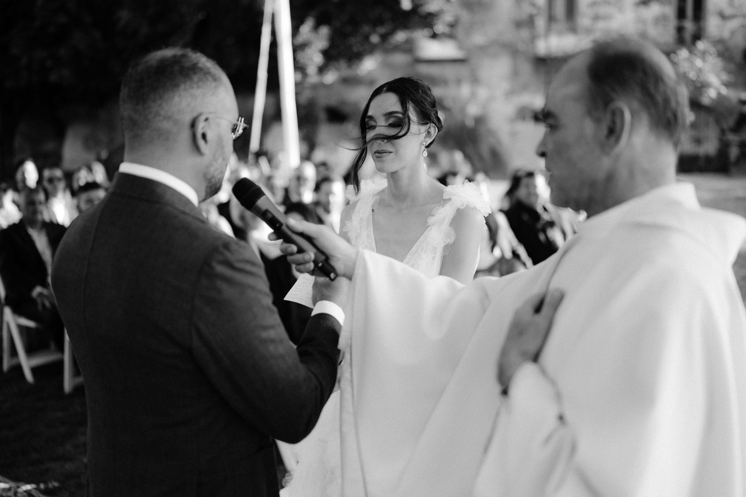 Black and white photo of bride and groom exchanging vows with officiant at evening wedding ceremony.