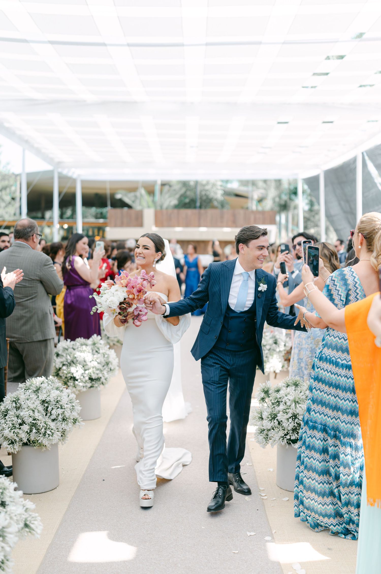 Joyful bride and groom walking down aisle after wedding ceremony surrounded by cheering guests.
