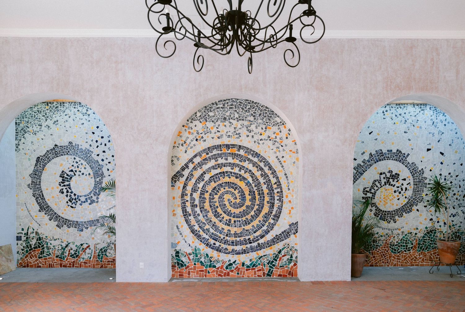 Decorative mosaic spiral artwork in three arched niches on a white wall with chandelier above.