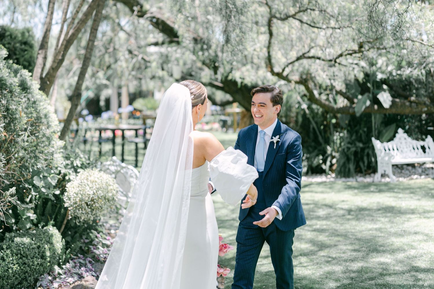 Groom smiling at bride in white wedding dress and veil during first look outdoors.