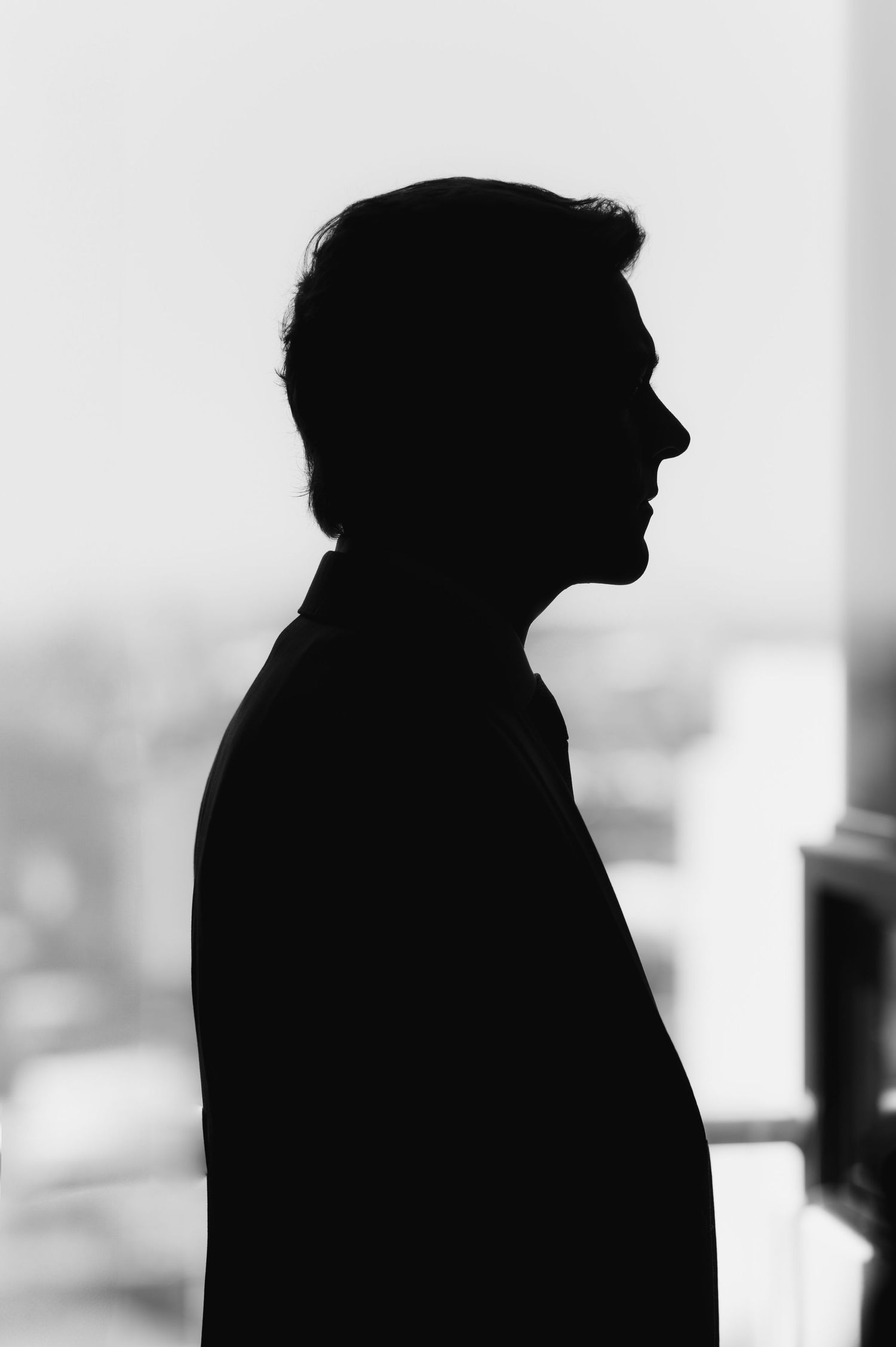 Dramatic black and white silhouette portrait of a man in profile against a bright window.
