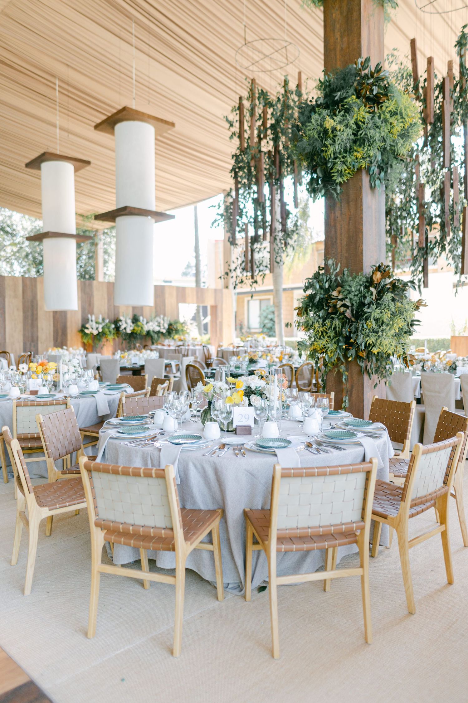 Wedding reception tables set with gray linens, rattan chairs, and lush hanging greenery.