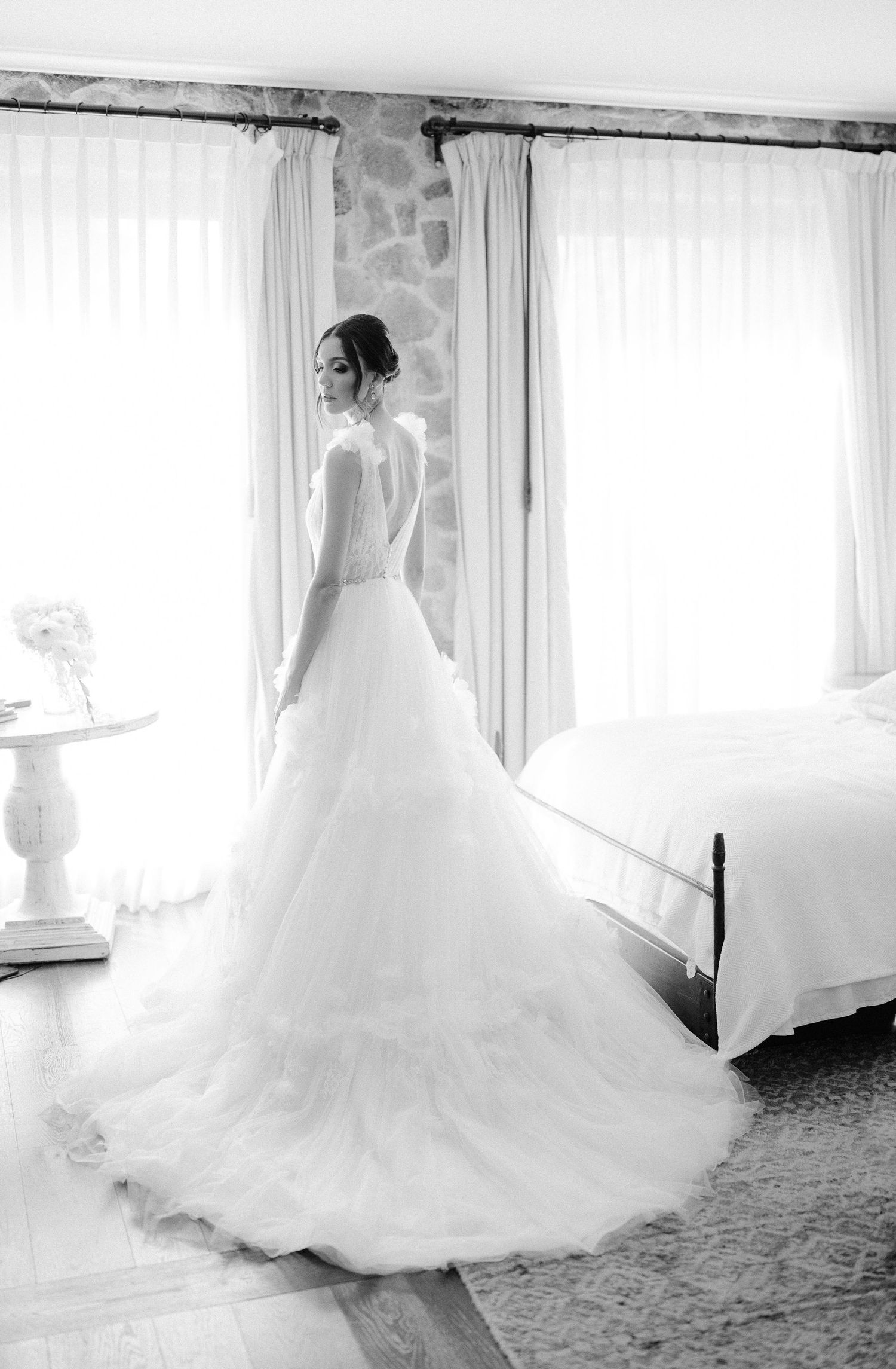 Black and white portrait of bride in ball gown with long train by window.