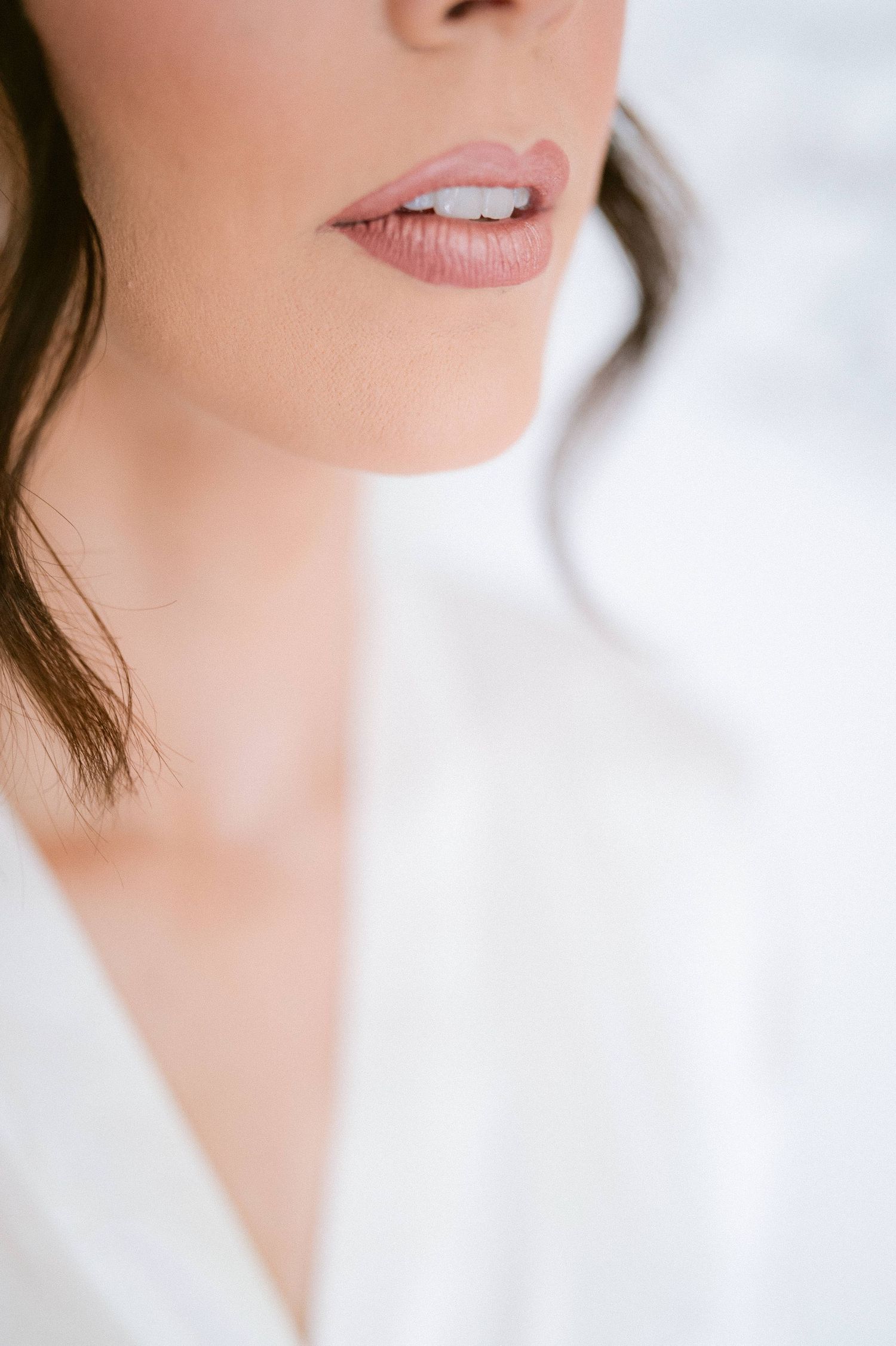 Close-up of bride's lips with nude pink lipstick and white teeth in a soft white bridal robe.
