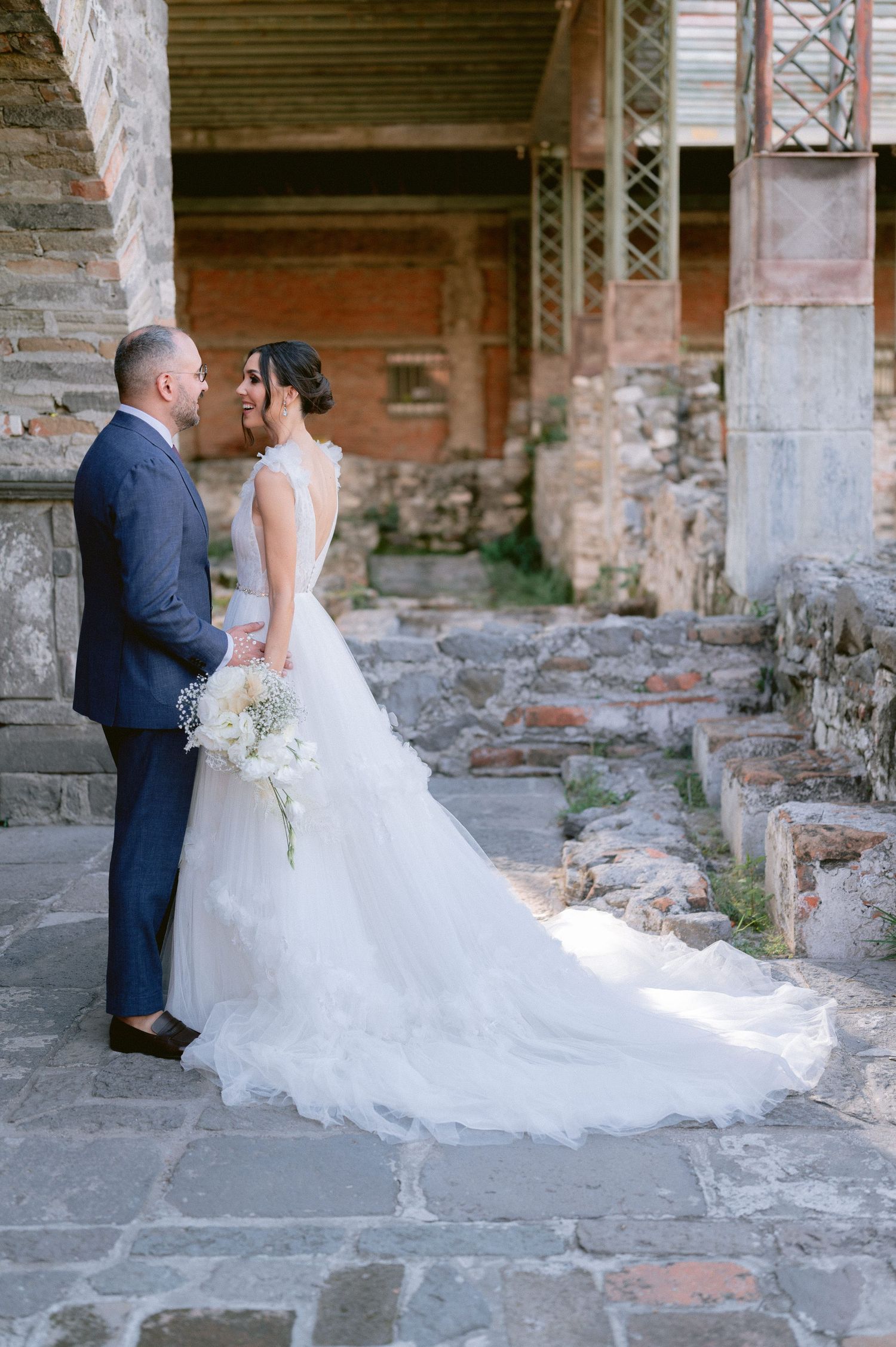 Bride and groom share an intimate moment standing close together on stone pavement at ruins venue.