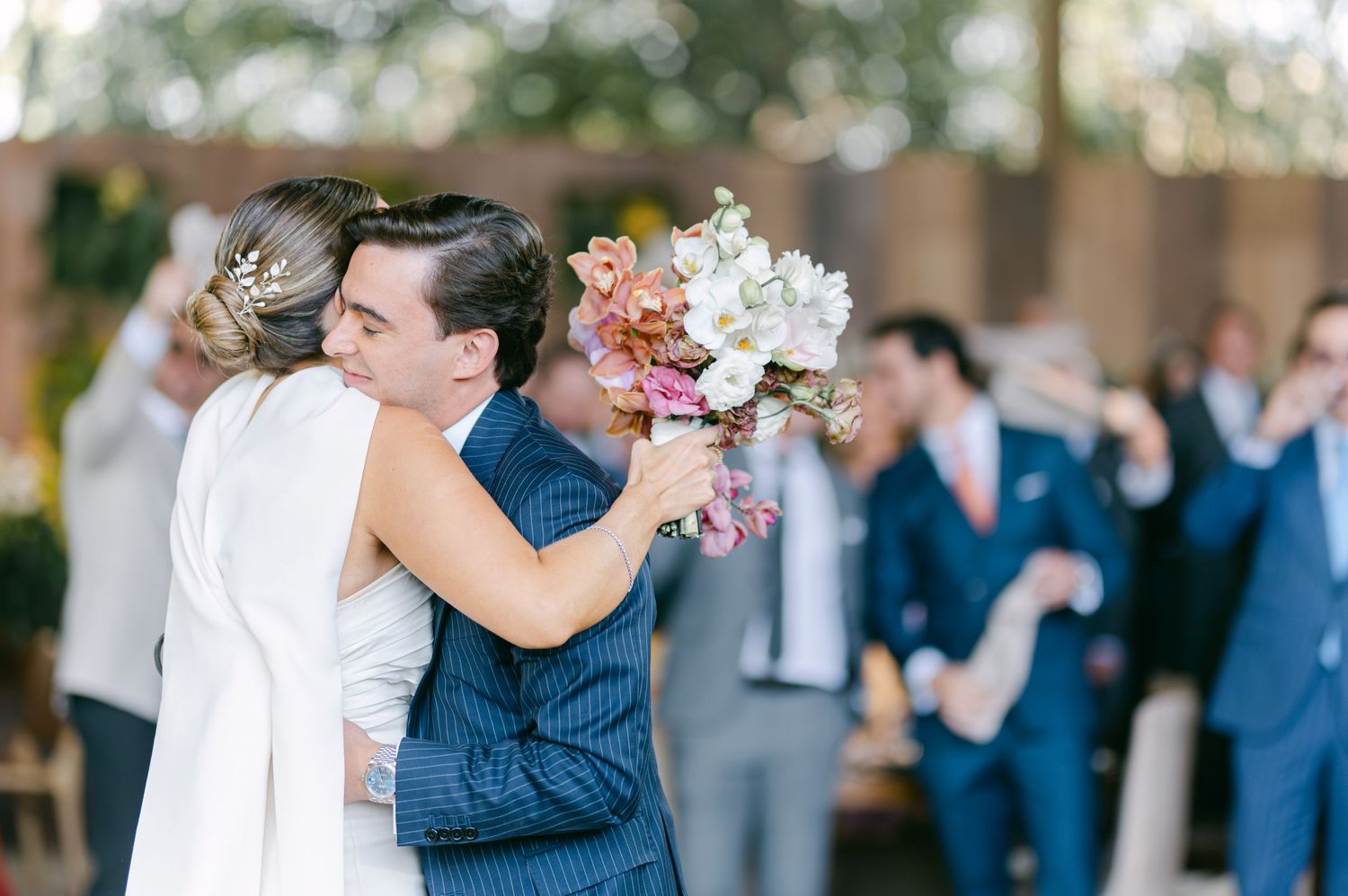 Groom embracing bride in heartfelt hug while she holds colorful bridal bouquet after ceremony.