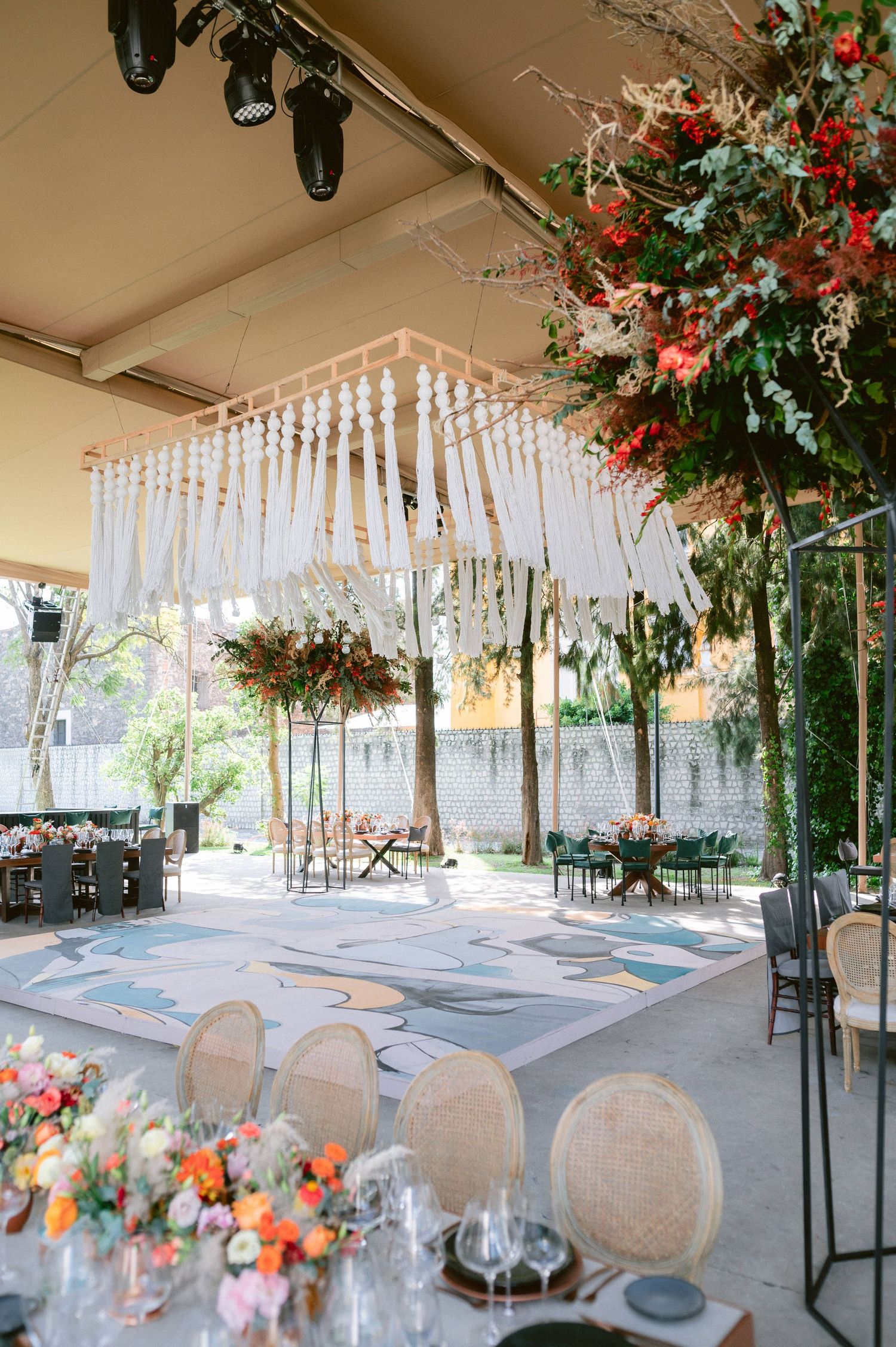 Wedding reception dance floor with macrame chandelier, colorful florals and cane back chairs.