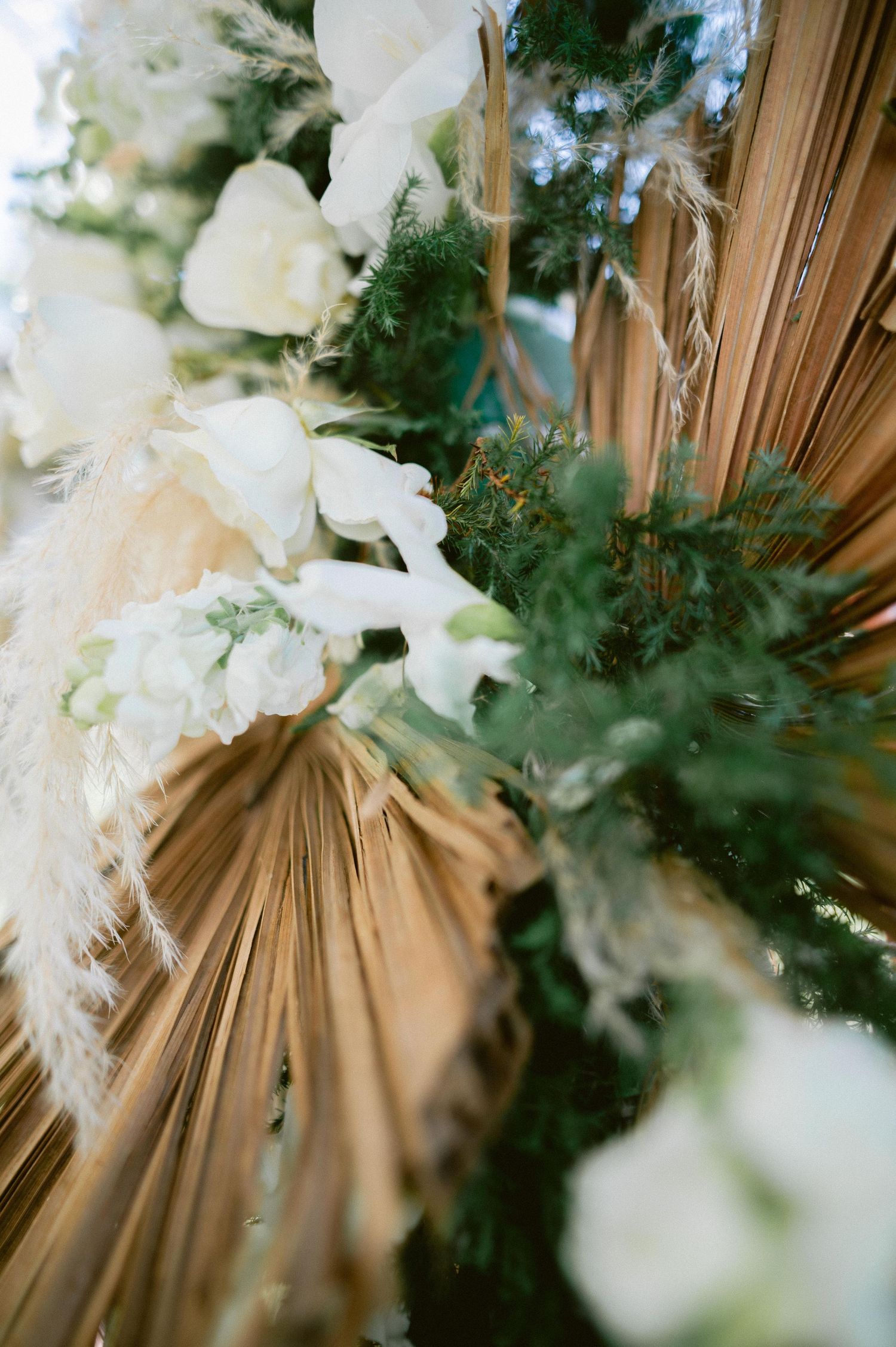 Close-up of bohemian wedding arch with dried palm leaves, white roses, and lush greenery florals.