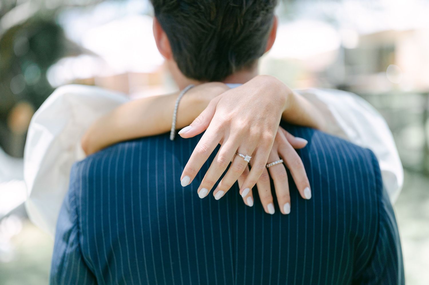 Close-up of bride's hand with diamond ring resting on groom's navy pinstripe suit.