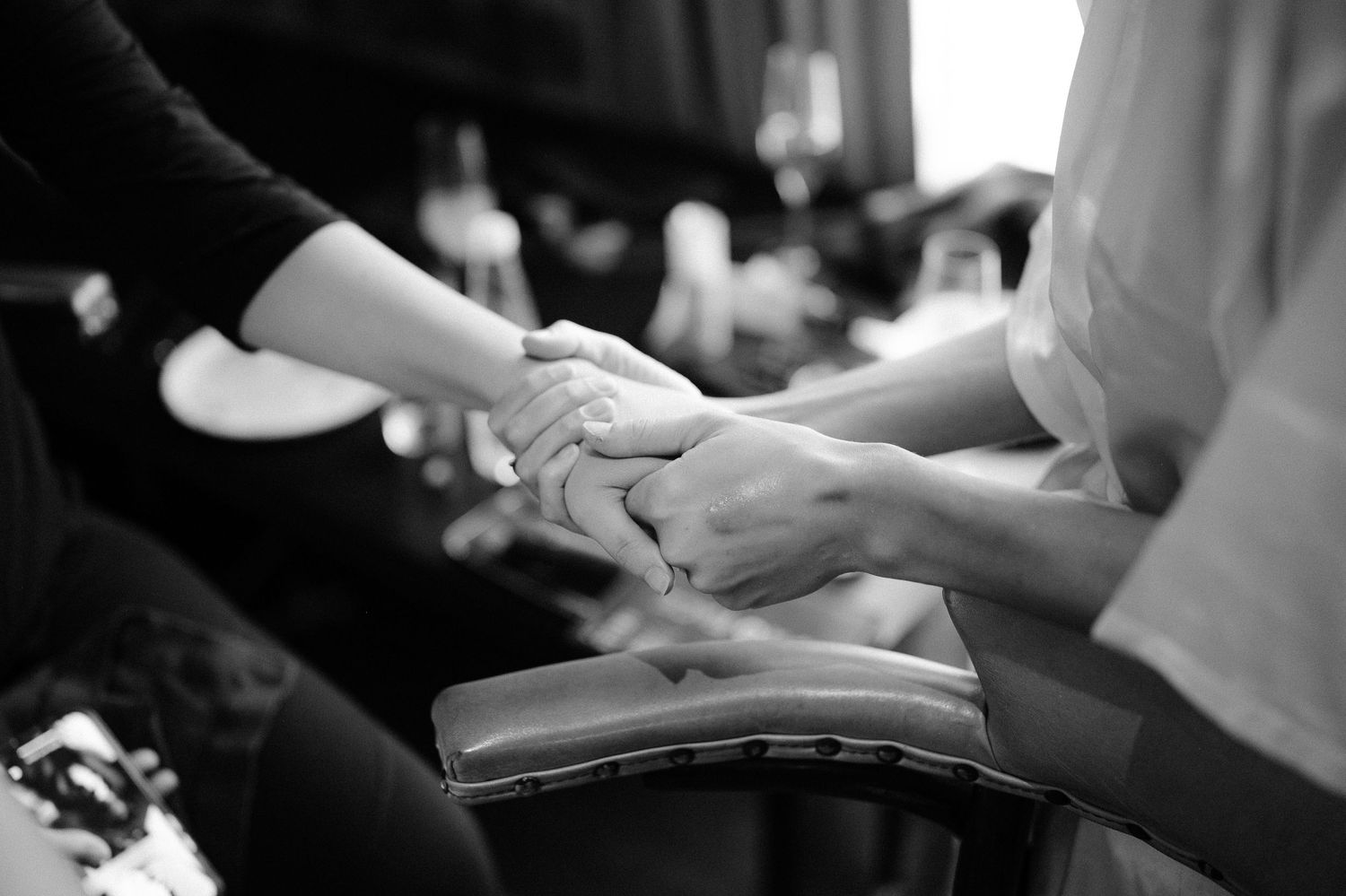 Close-up black and white photo of hands being held tenderly during bridal preparations.