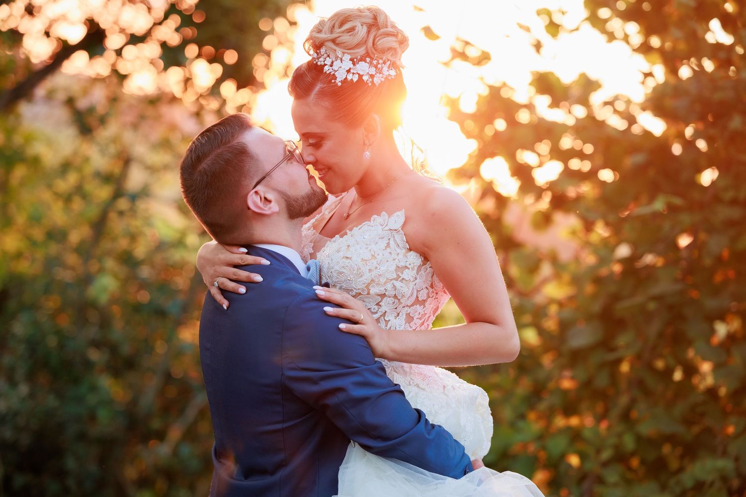 A romantic wedding couple embraces in beautiful golden sunset light filtering through trees.