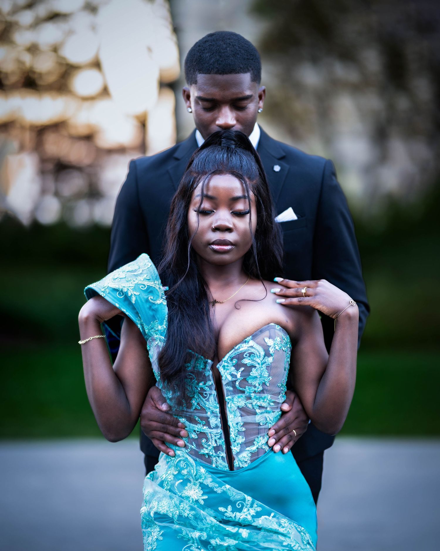 A romantic couple in formal attire share an intimate moment in a blue evening gown and black suit outdoors at dusk.