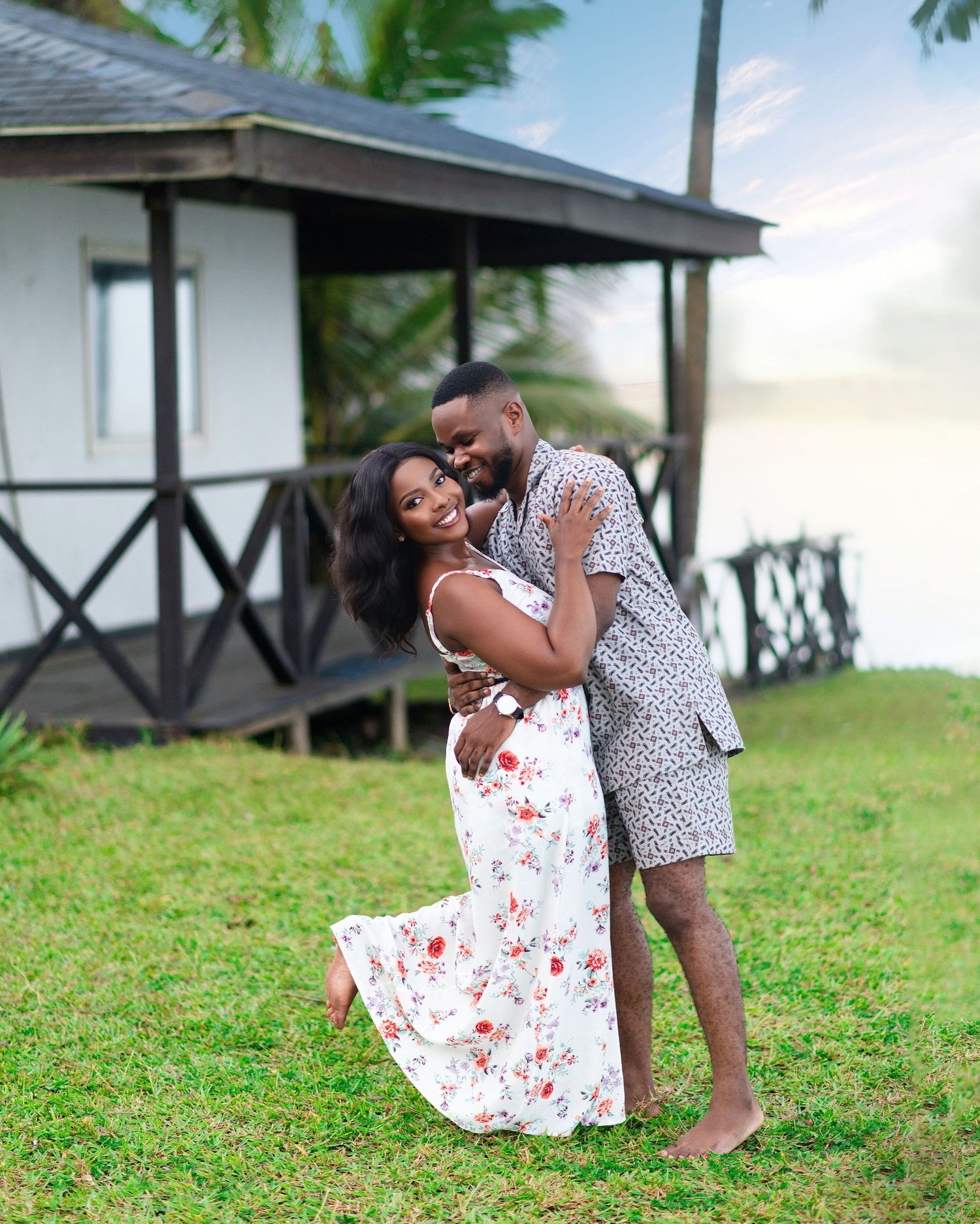A couple shares a romantic moment together on a grassy lawn with small buildings in the background.