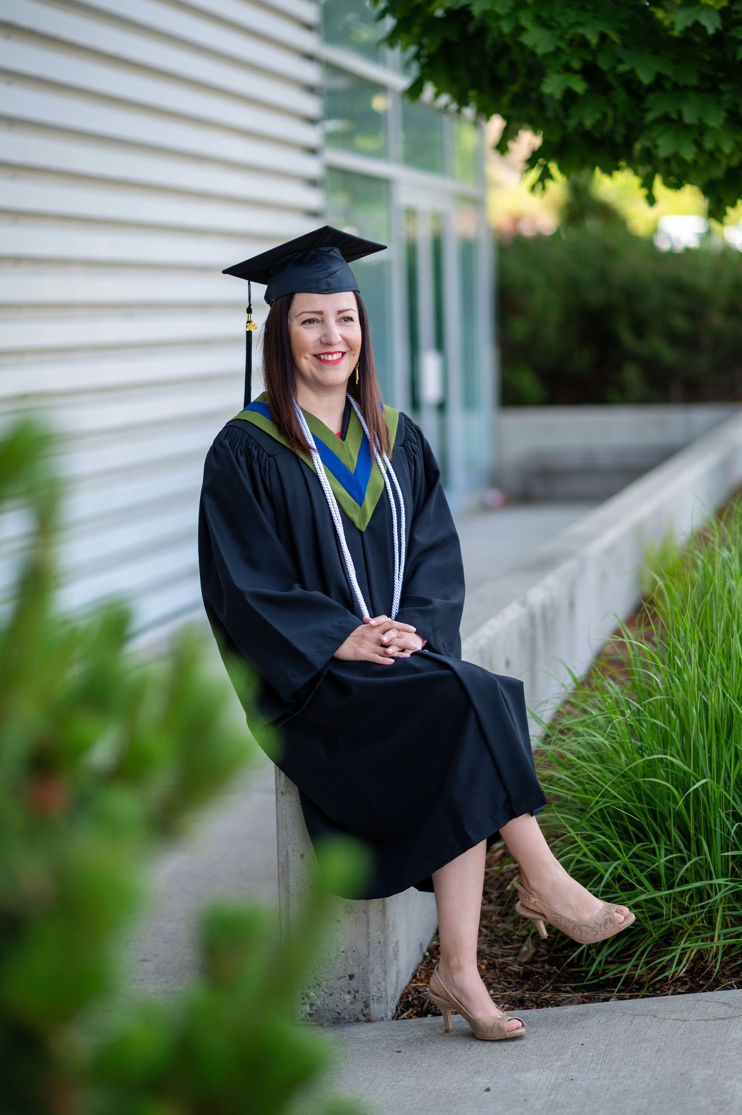 Graduate in traditional academic regalia sits casually on concrete steps outdoors.