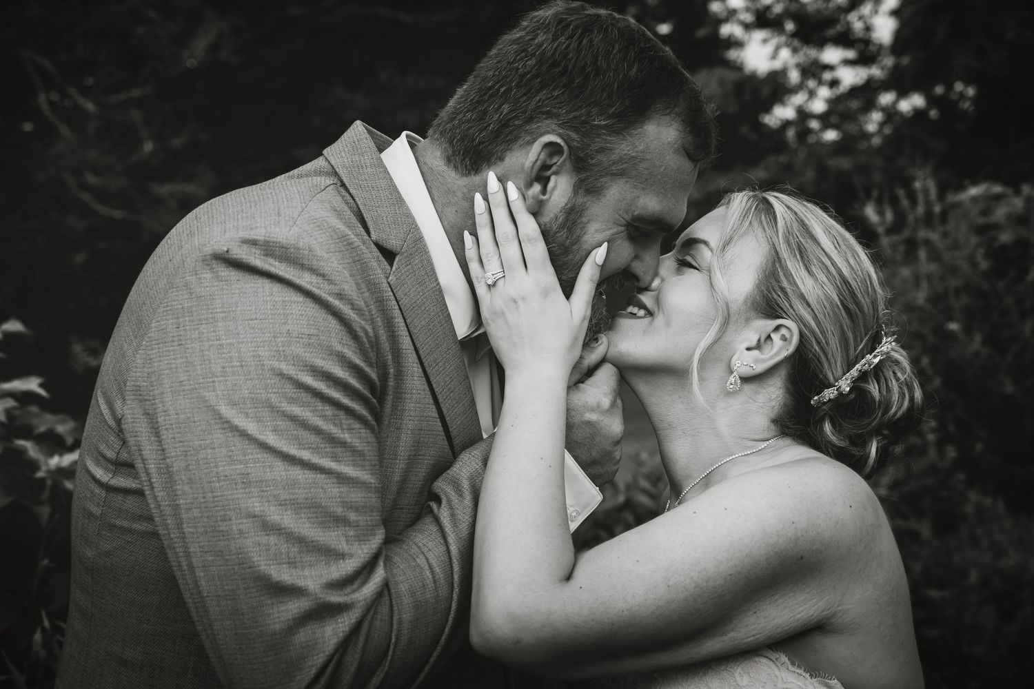 Black and white wedding photo of a smiling bride and groom sharing an intimate moment, foreheads touching outdoors.