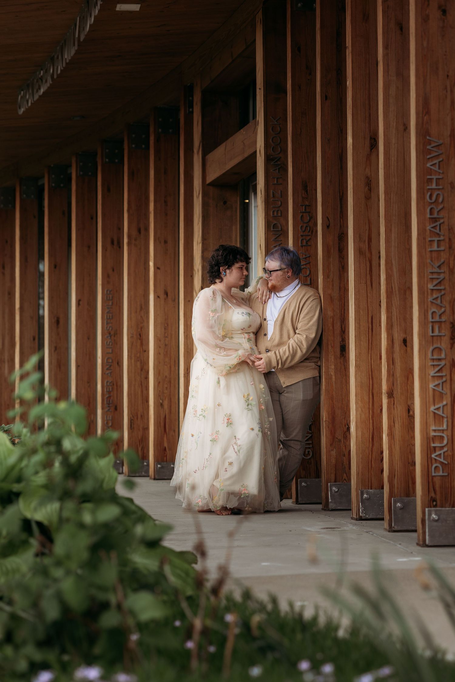Paula and Frank Harshaw share a romantic moment in wedding attire against a wooden building backdrop.