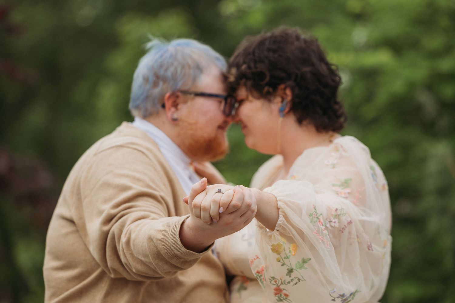 Elderly couple holding hands and sharing a tender moment outdoors, surrounded by lush green foliage.