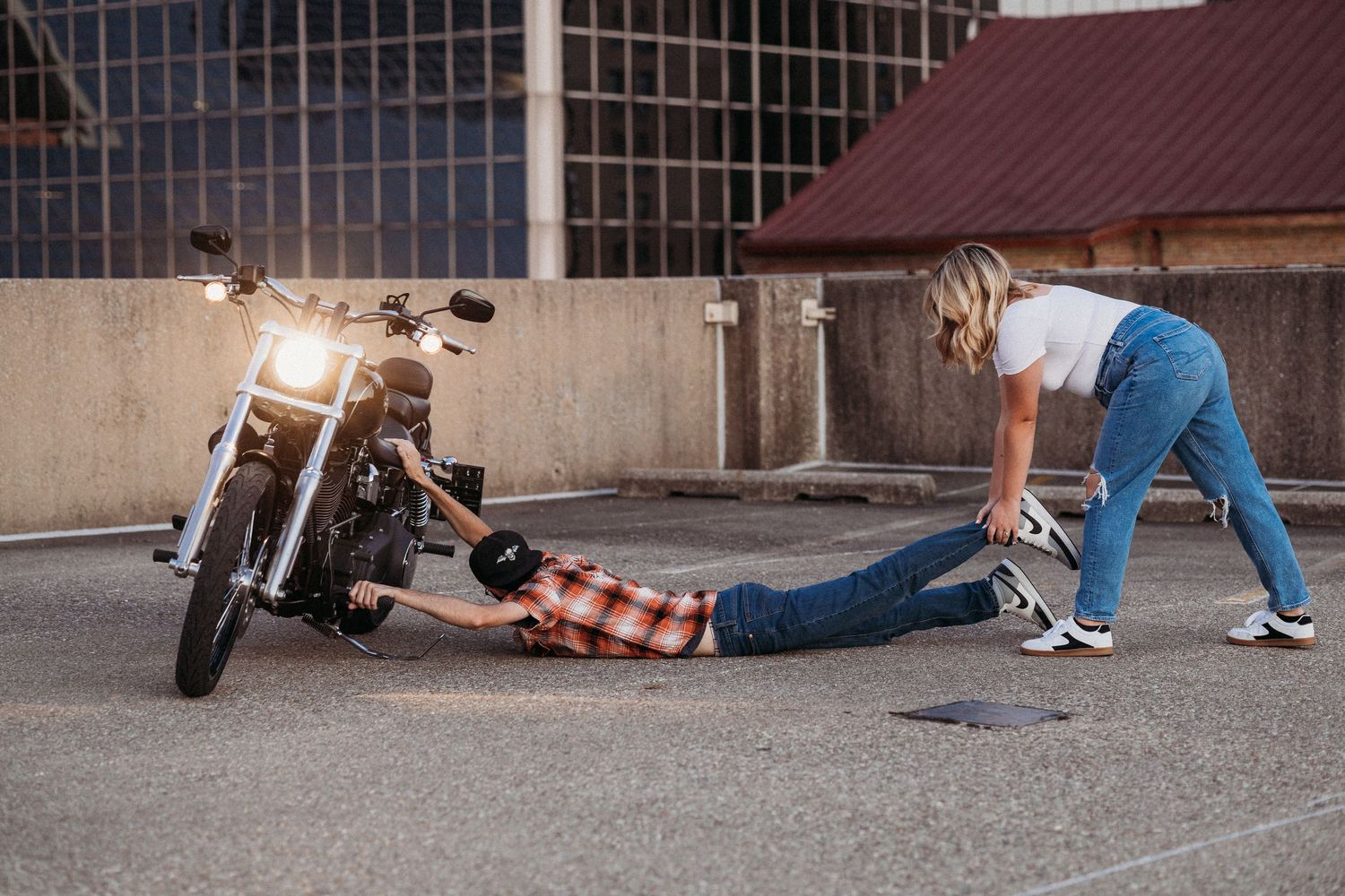 Woman helping man lying on ground next to a parked motorcycle in an urban parking area at night.