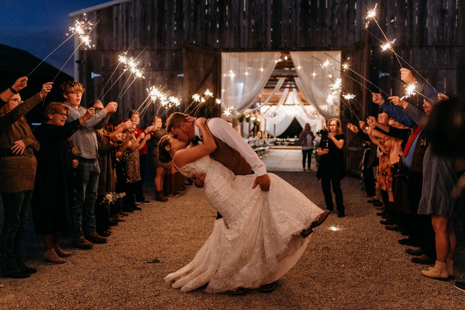 Bride and groom sharing romantic dip kiss during sparkler send-off exit at night wedding reception.