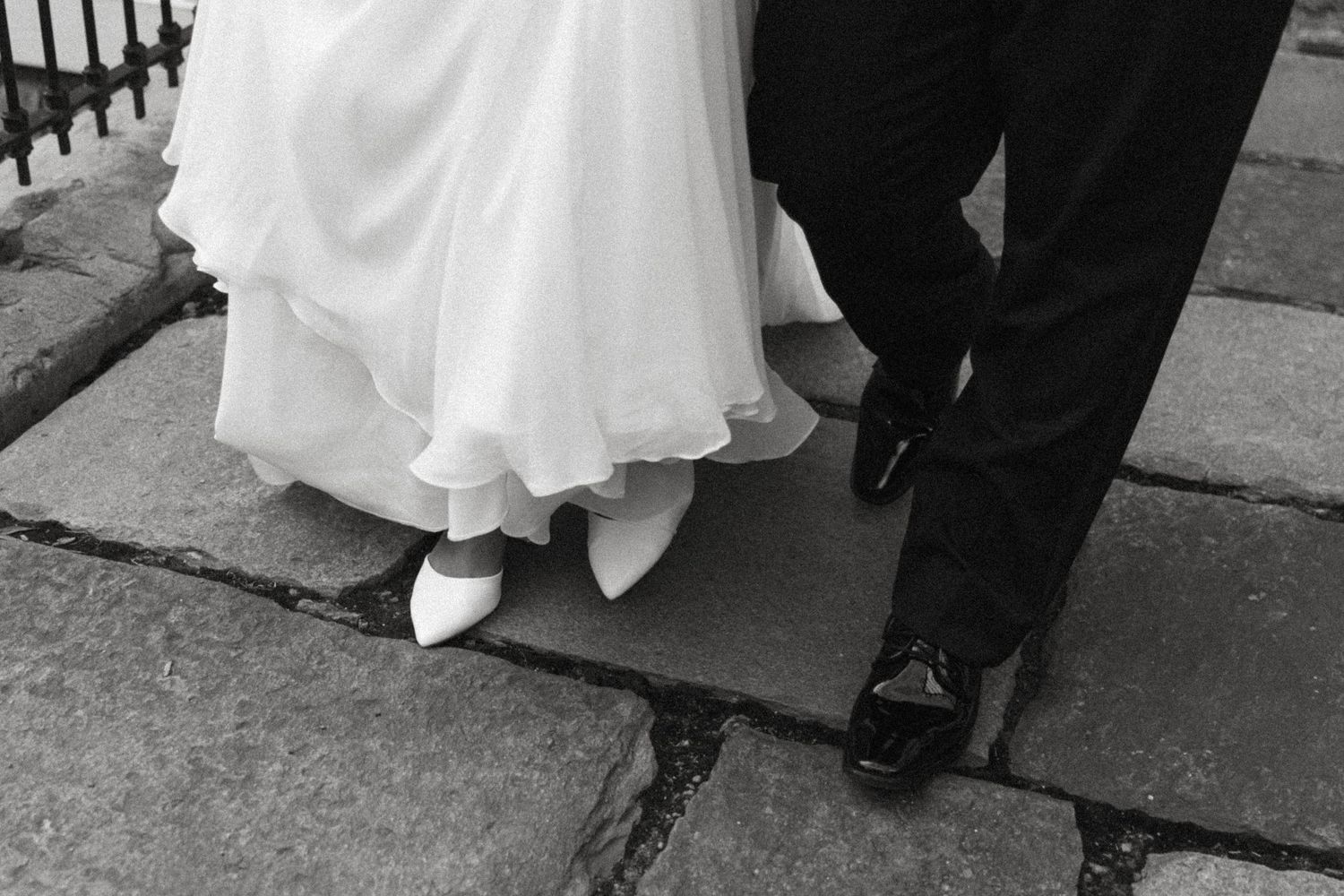 Close-up black and white shot of bride and groom's feet on stone pavement during their wedding.