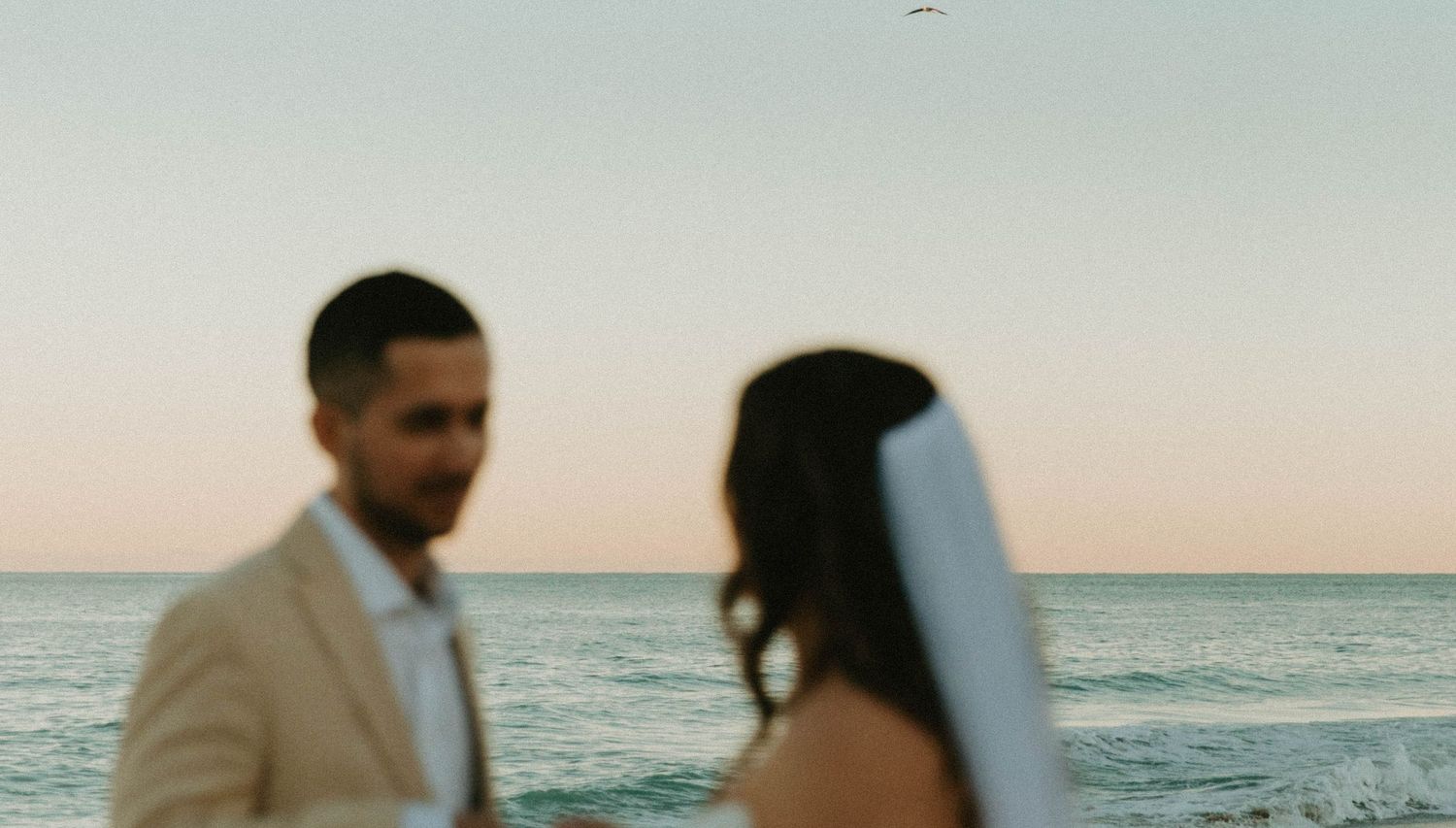 Couple shares intimate moment on beach during golden hour with ocean horizon behind them.