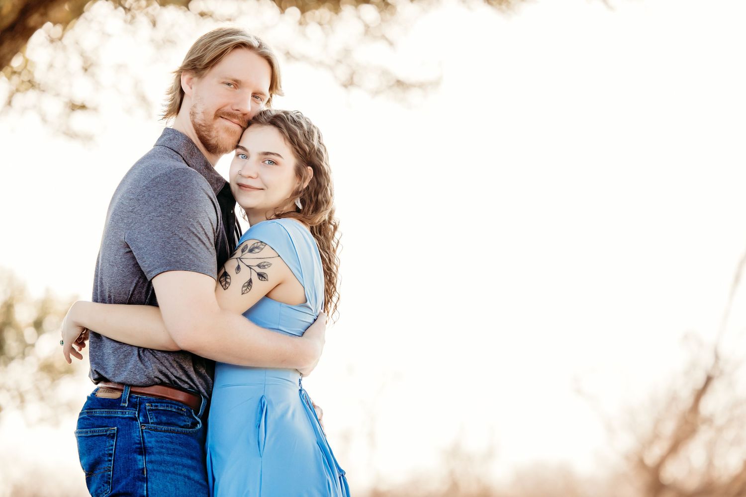 A couple embraces in a romantic outdoor engagement photoshoot with soft sunlit lighting and natural scenery in Fort Worth.