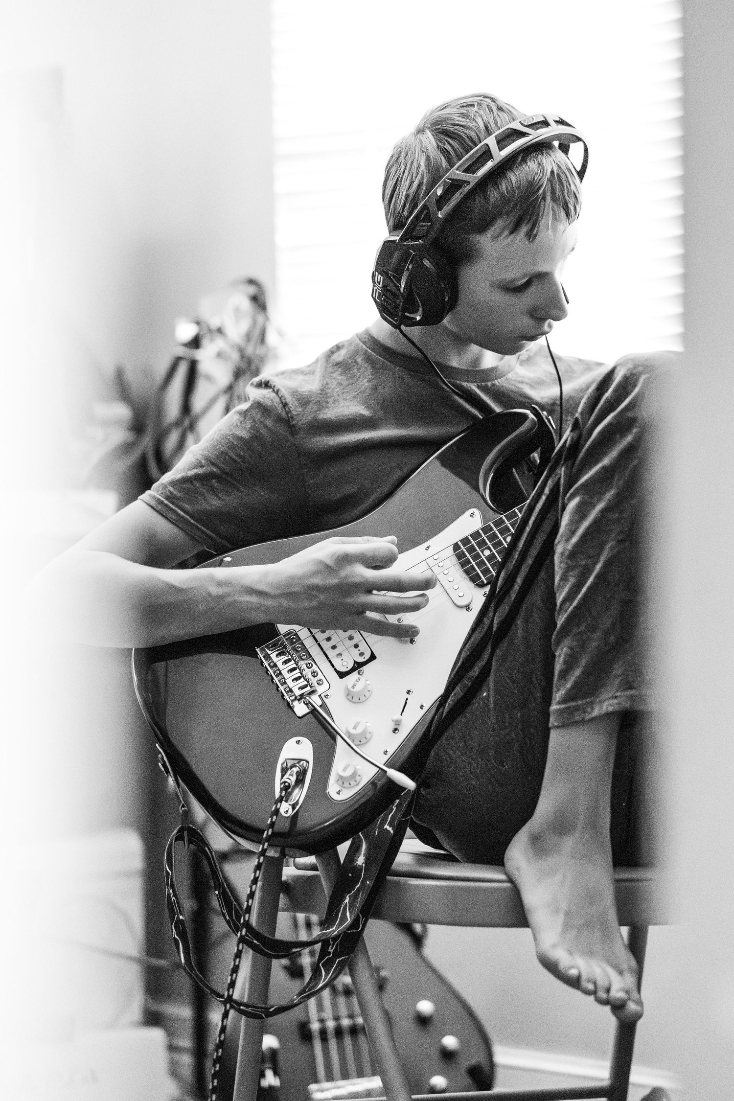 Black and white photo of a musician wearing headphones while playing an electric guitar in a studio setting.