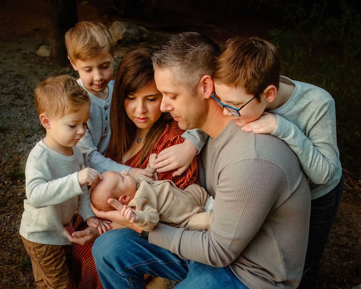 Family members sit close together around newborn baby outdoors during golden hour lighting in Keller, TX.