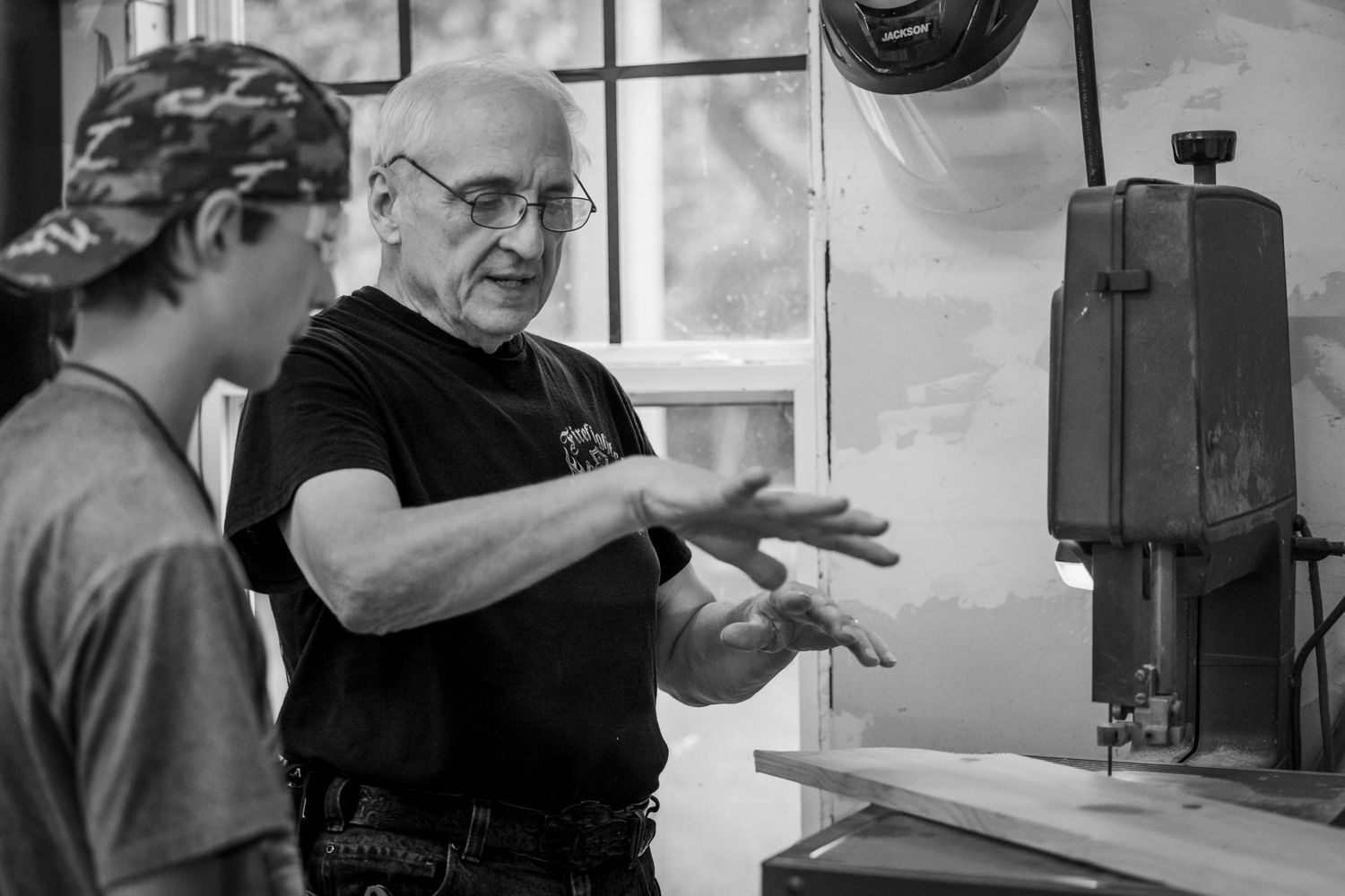 Two people engaged in discussion near workshop equipment in black and white photograph.