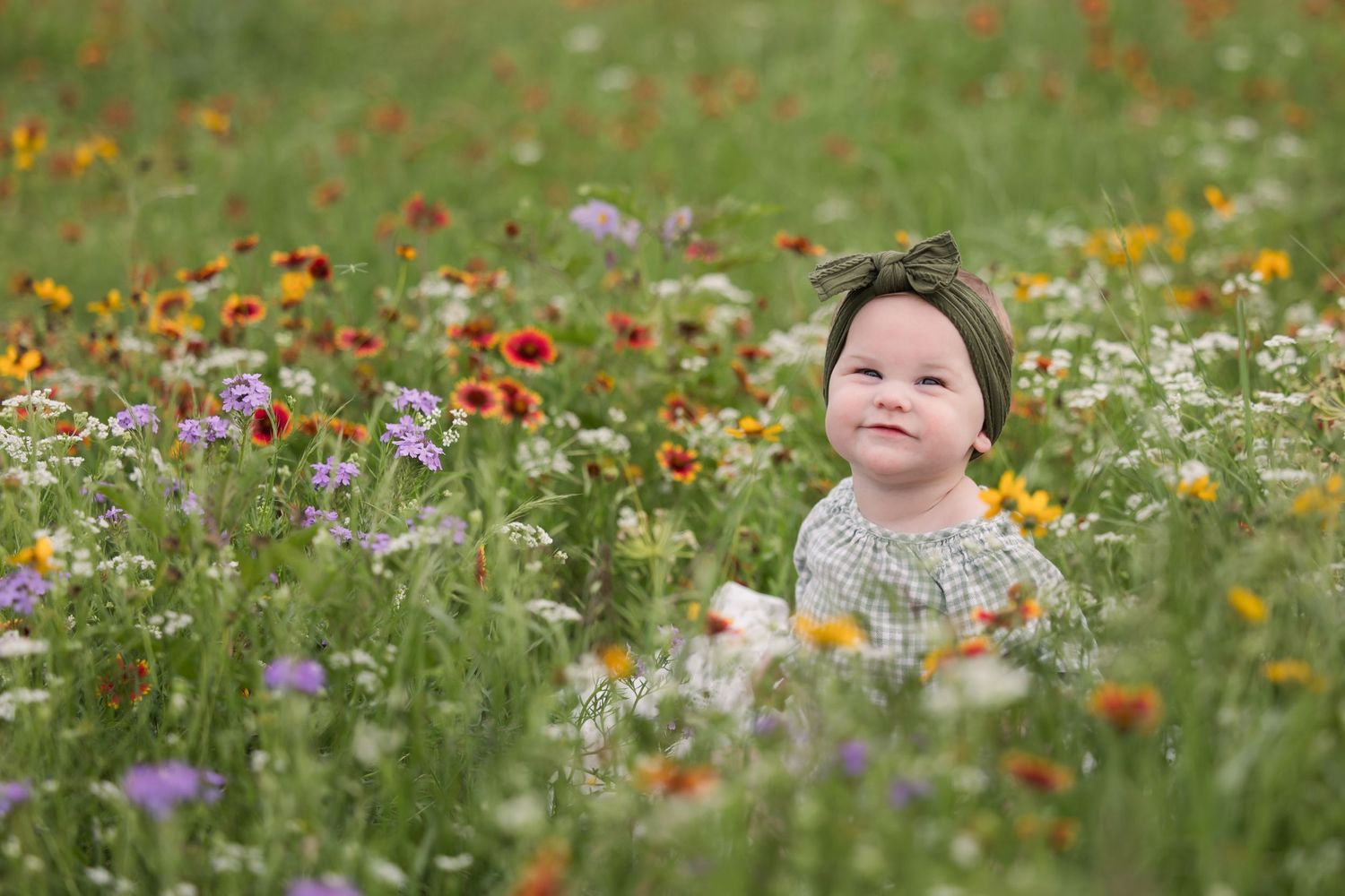 Small figure sits among colorful wildflowers in a meadow on a bright summer day.