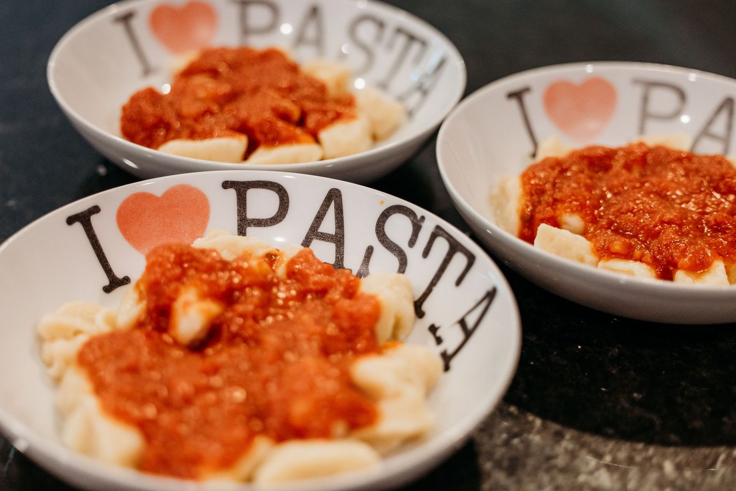 Small white plates with heart logos serving pasta topped with bright red tomato sauce and melted cheese.