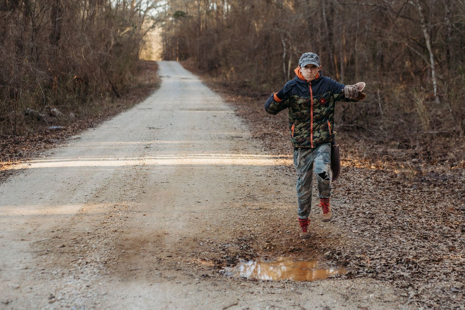A meandering dirt trail winds through a winter forest with bare trees and brown foliage on both sides.