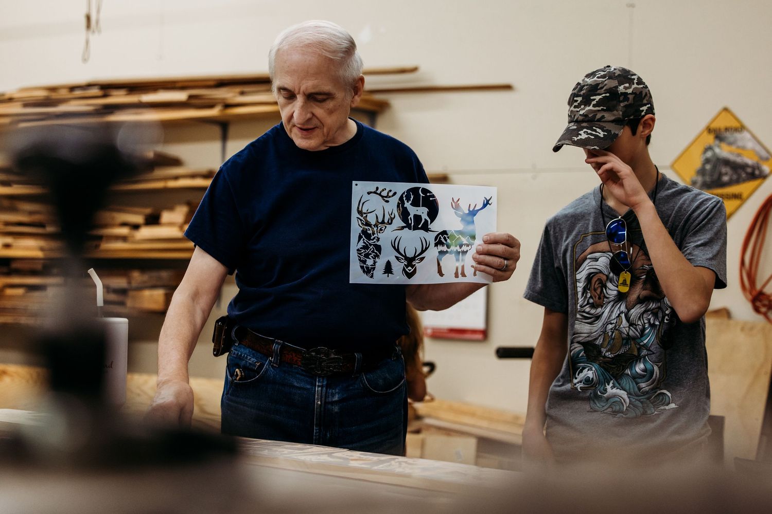 Person holding wood samples in a woodworking workshop while displaying prints for a collaborative creative project.